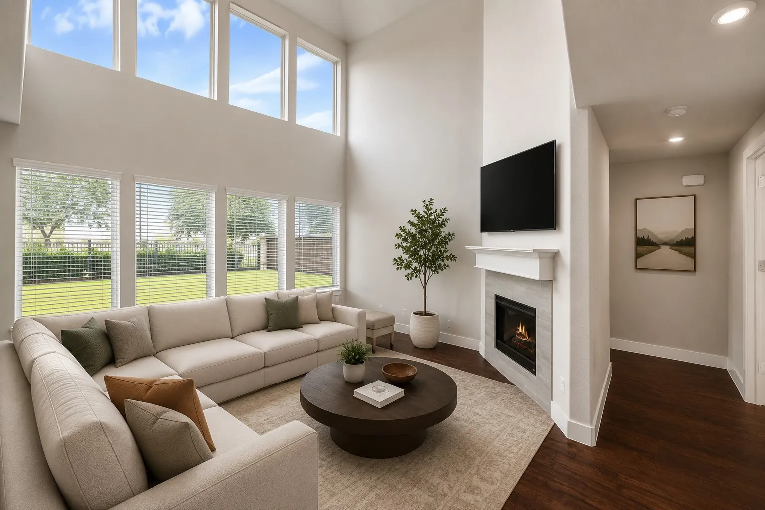 Living area with high ceilings, abundant natural light from multiple windows, a gas fireplace with a tiled surround, and dark wood-finish flooring
