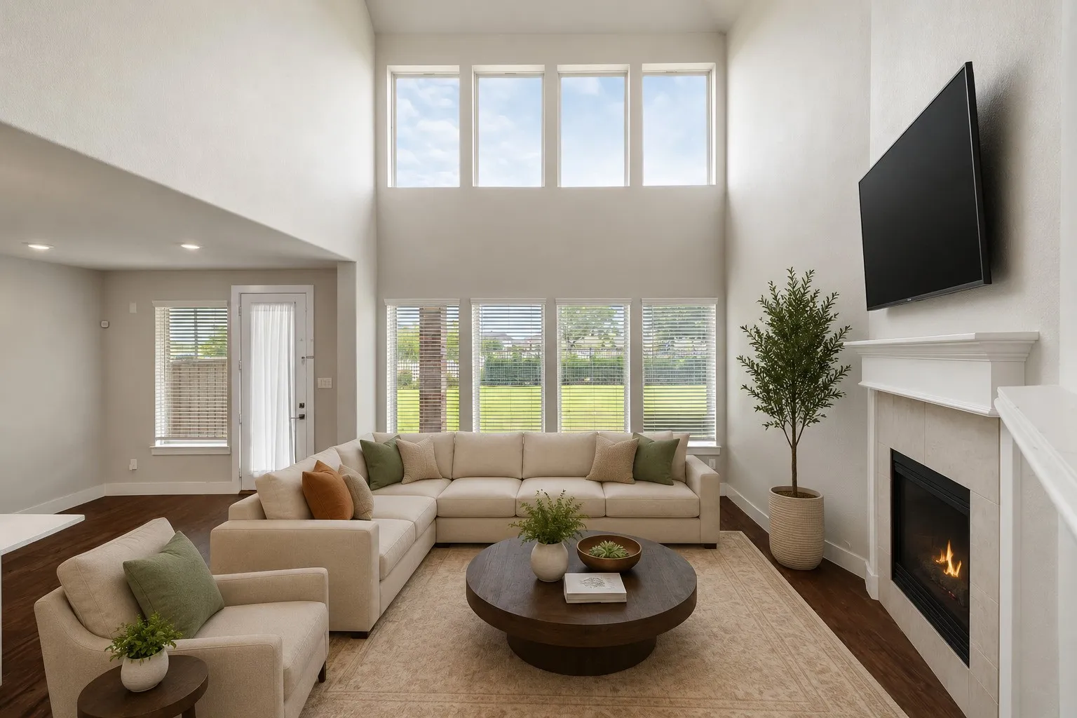 Open-concept living area featuring a two-story ceiling, multiple large windows, wood-finish flooring, and a fireplace with a mantel