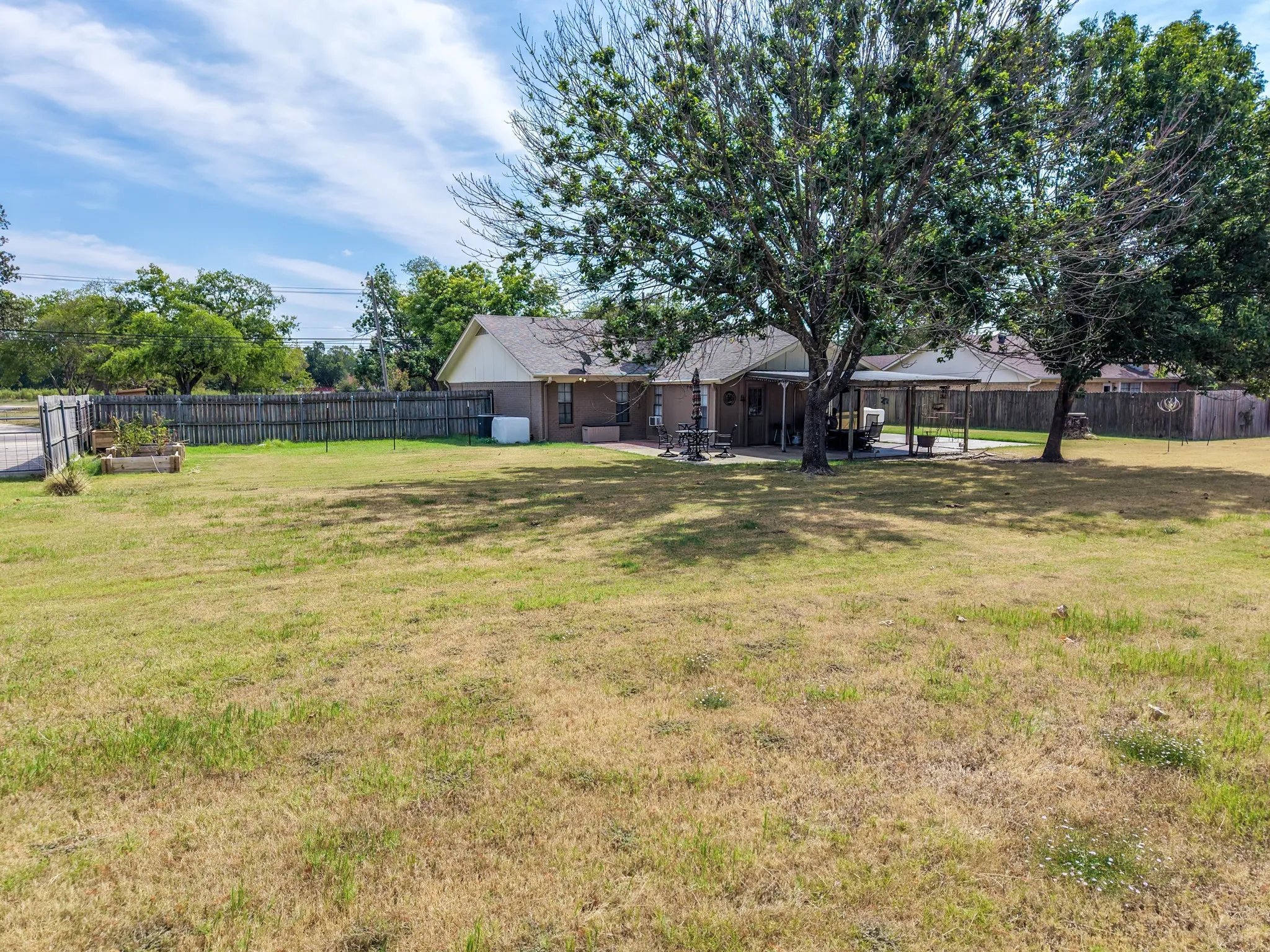 Expansive lawn area with a fenced perimeter, mature trees, and an attached covered patio