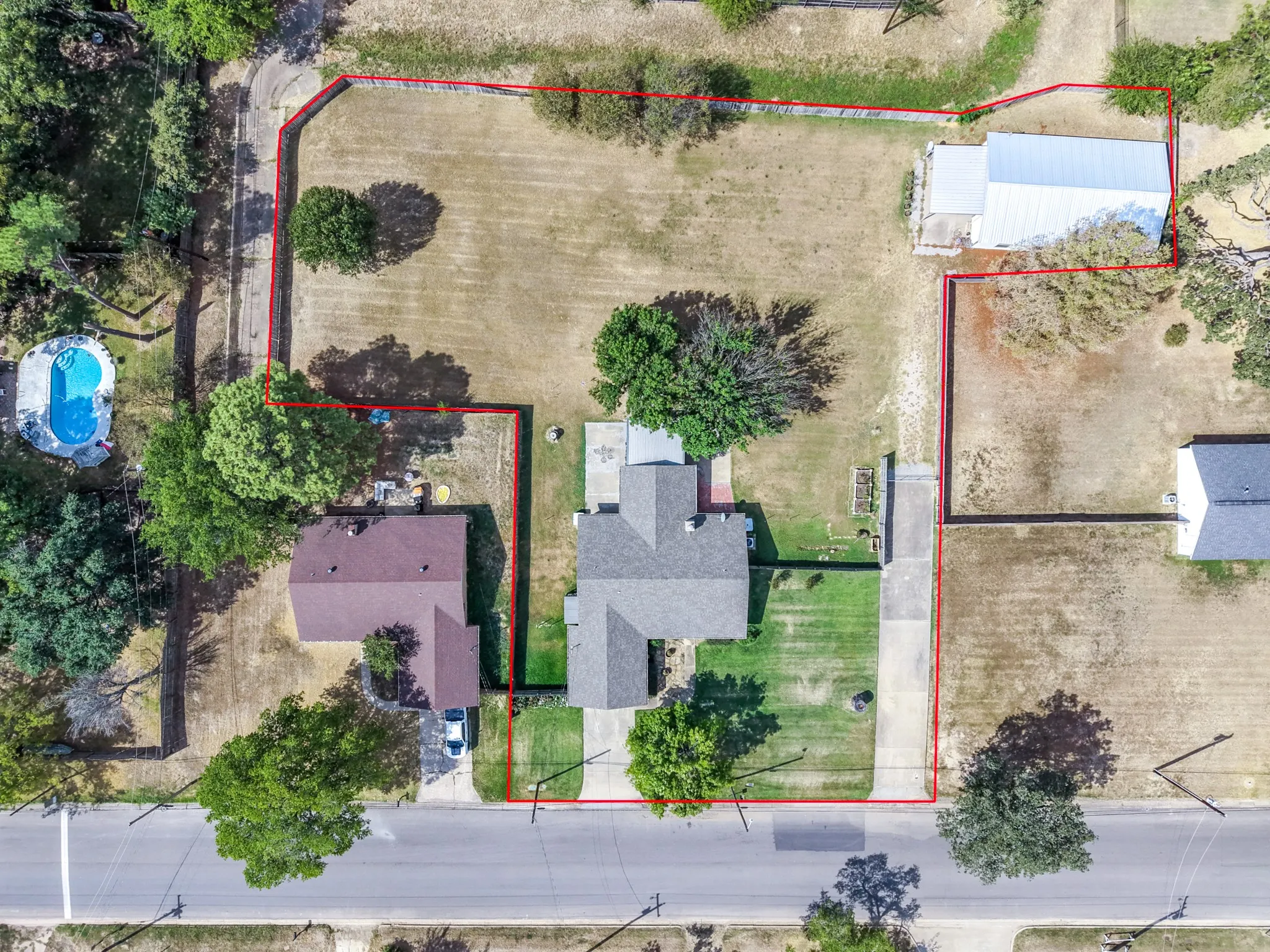 Expansive lot with mature trees, a long driveway, a detached building, and a separate structure with a light-colored roof