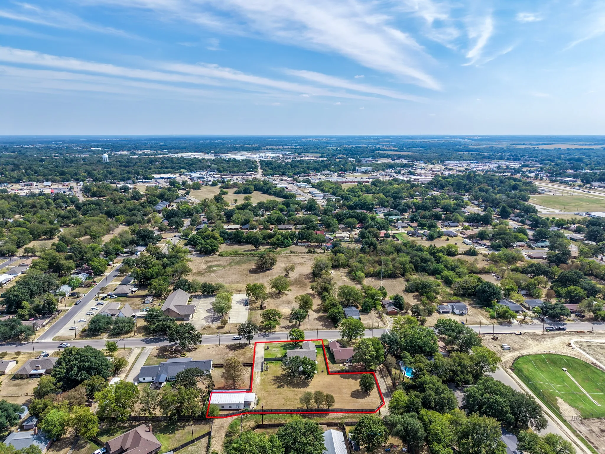 Aerial perspective showcasing a residential lot with mature trees and established structures, bordered by a paved road