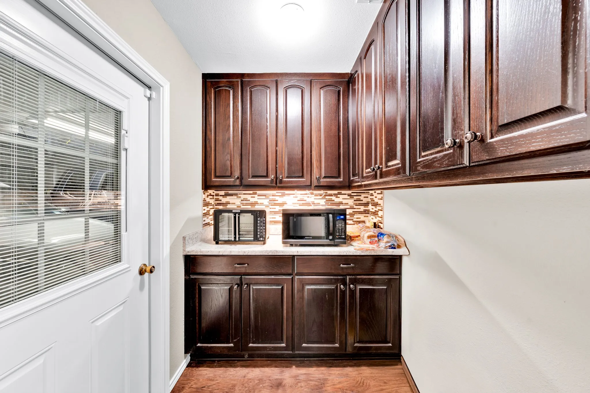 Dark wood-finish cabinetry, light-toned countertop, and a mosaic tile backsplash