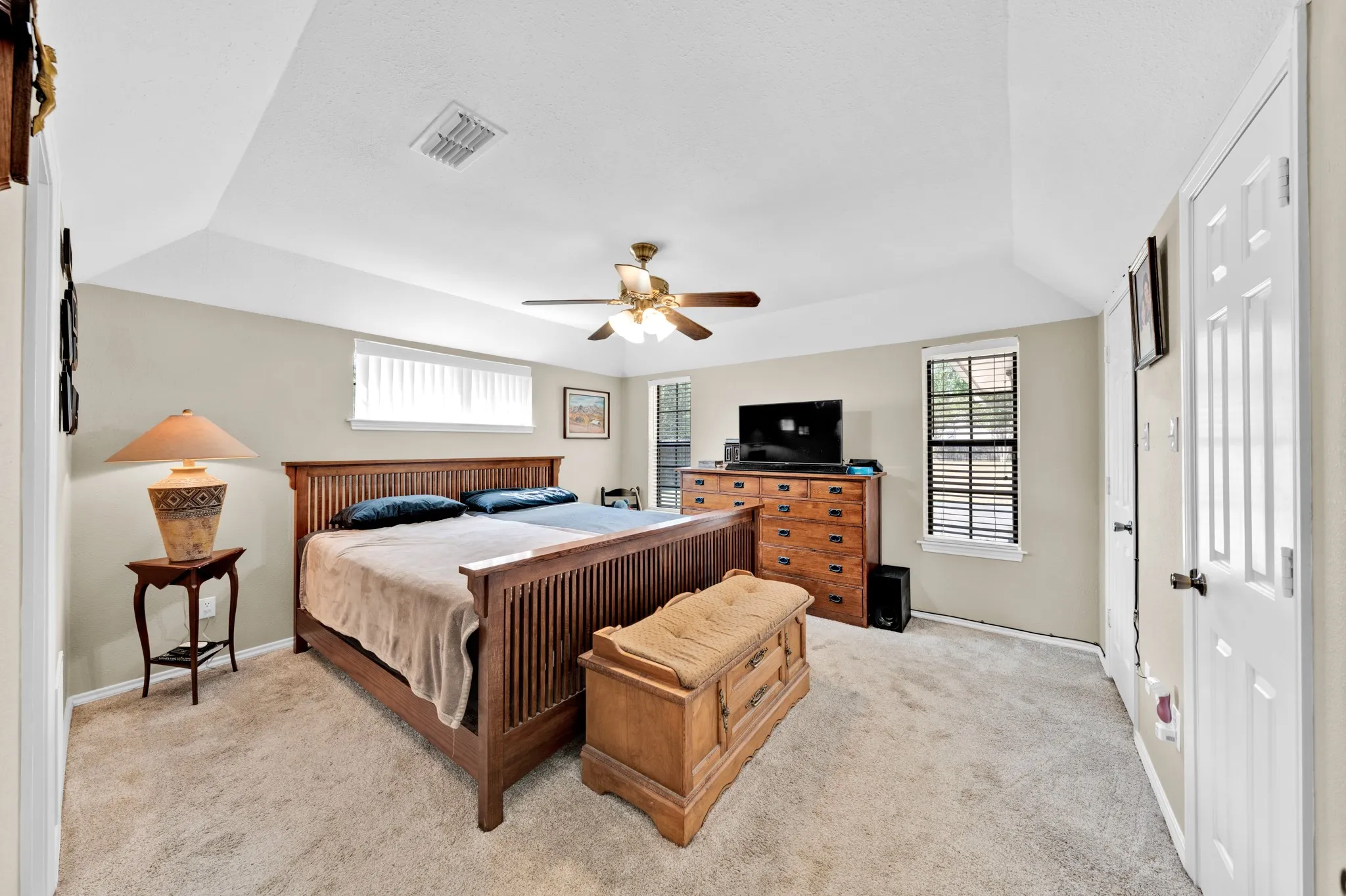 Tray ceiling with a ceiling fan, carpeted flooring, and multiple windows with blinds