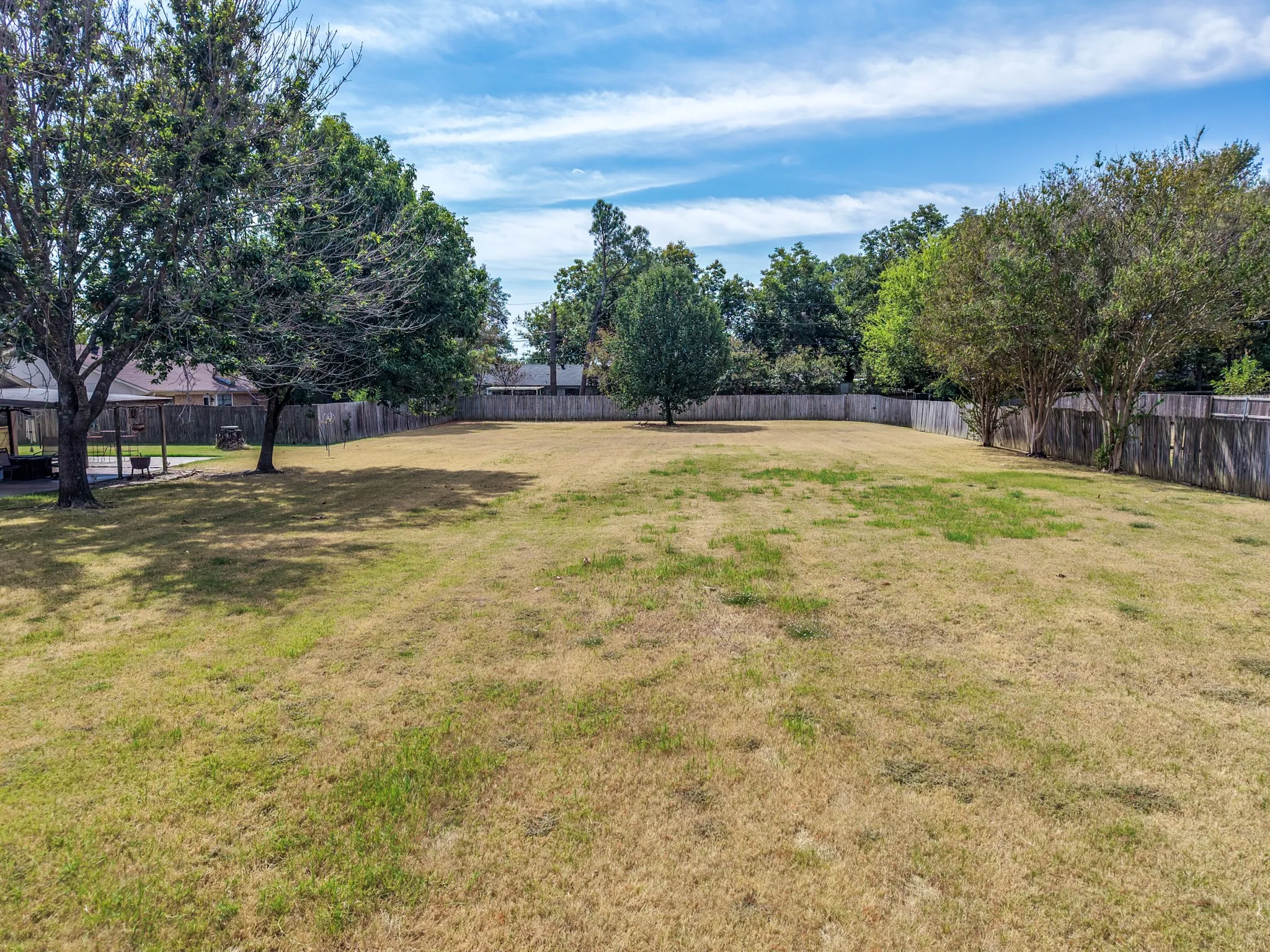 Expansive yard featuring a privacy fence, mature trees, and a detached gazebo