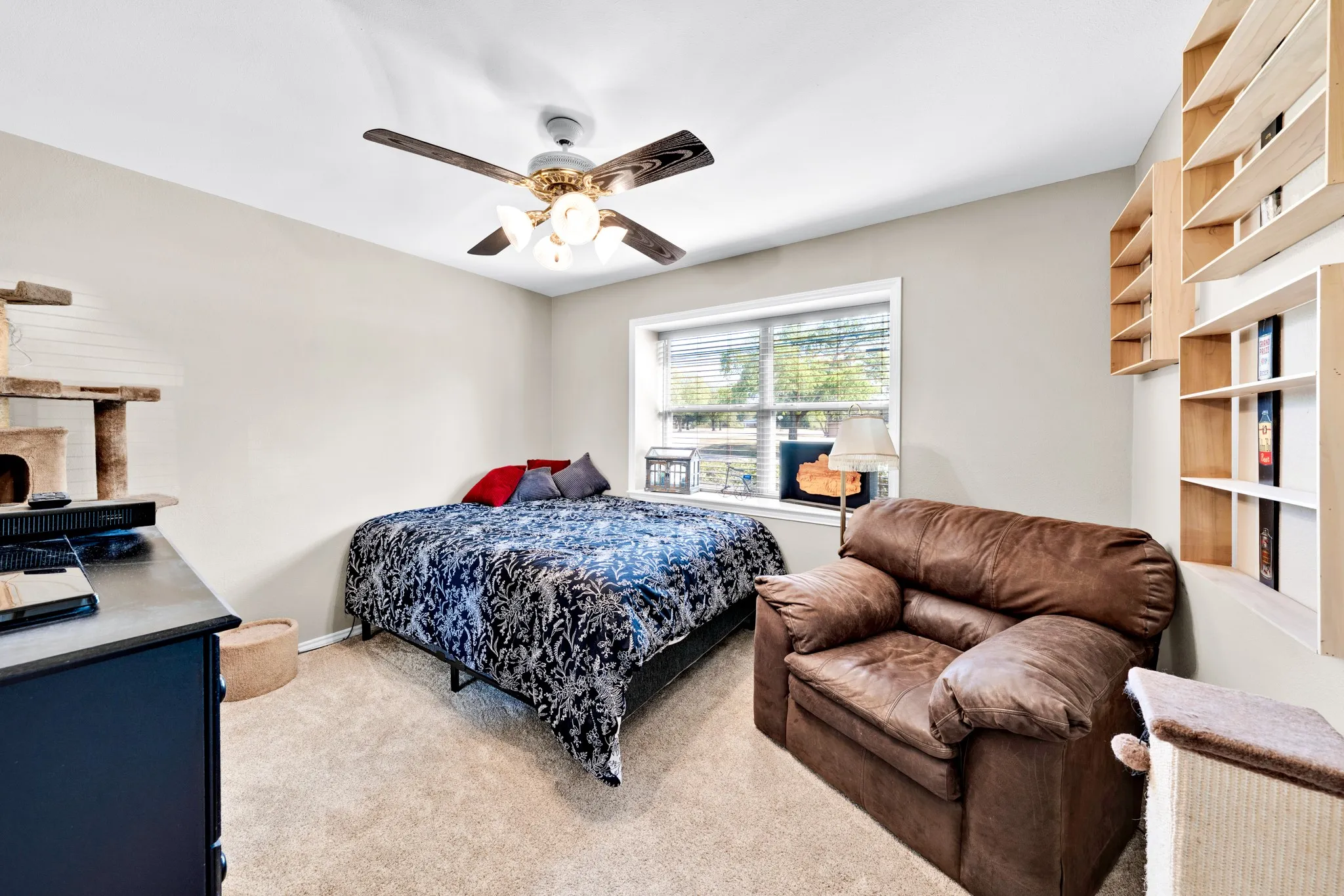 Carpeted room featuring a ceiling fan with integrated lighting, a window with blinds, and built-in wall shelving