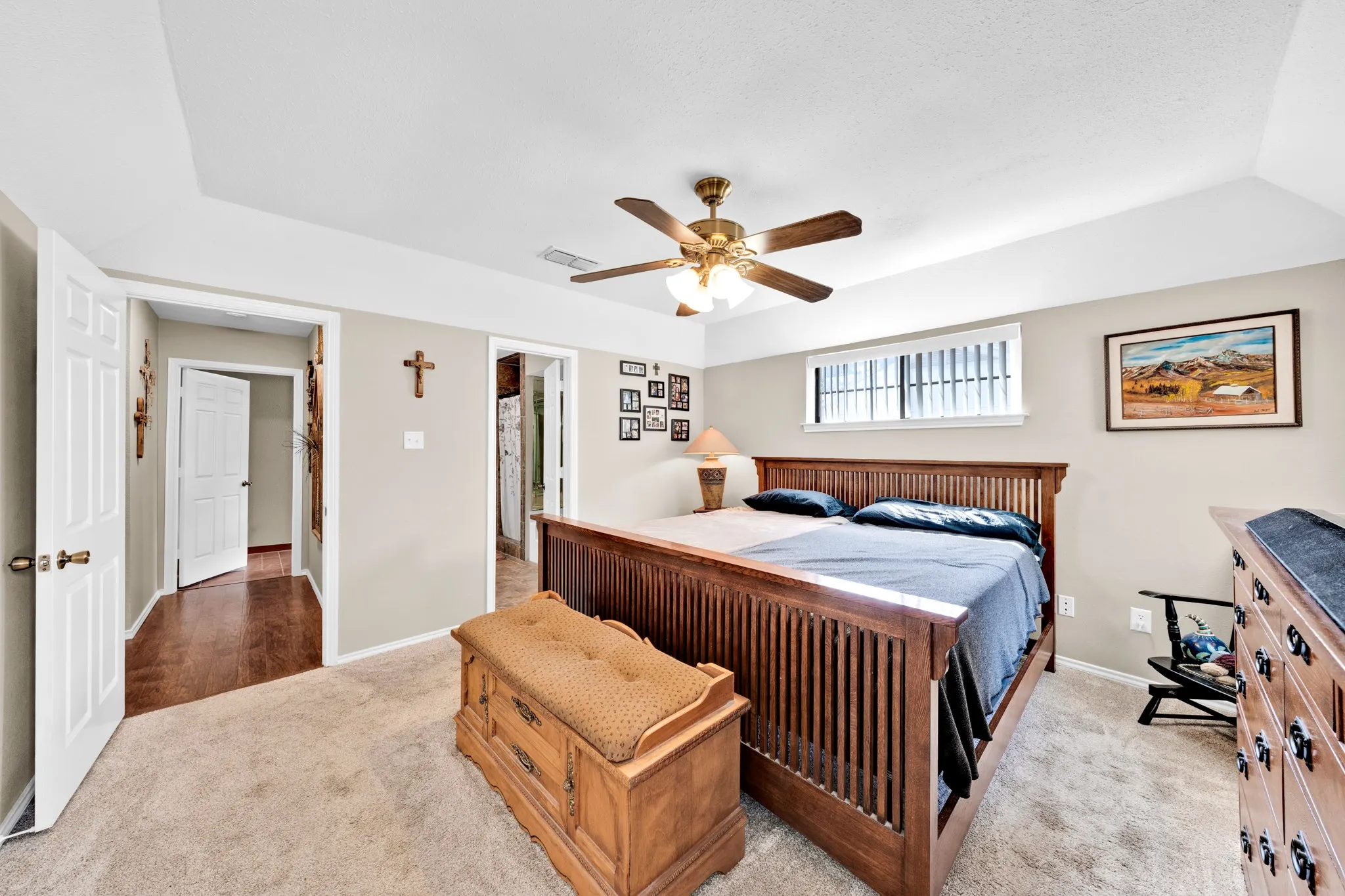 Tray ceiling with crown molding, carpeted flooring, window with blinds, wood-finish ceiling fan, and painted walls