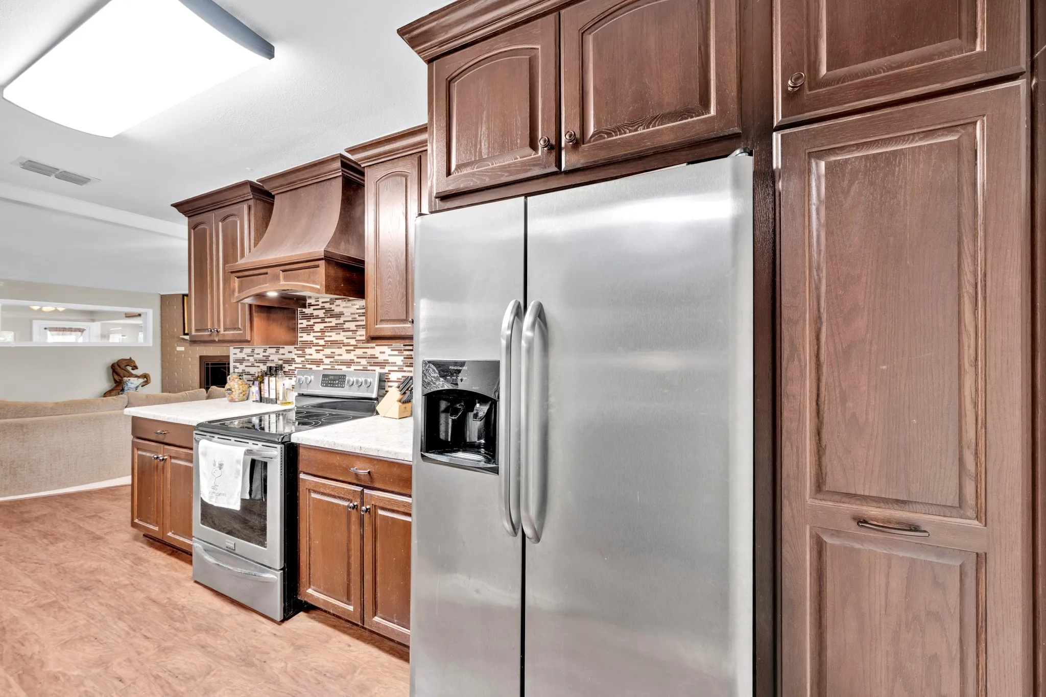 Wood-finish flooring with a stainless steel refrigerator, built-in range, and mosaic tile backsplash