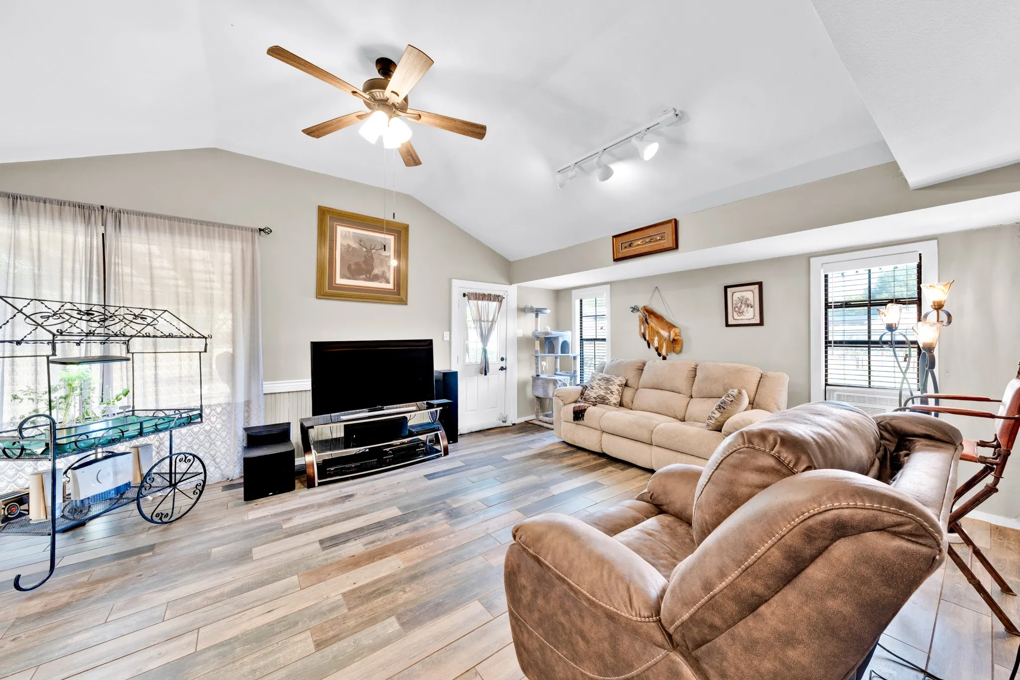 Vaulted ceiling with a ceiling fan, plank-style flooring, white trim, and track lighting