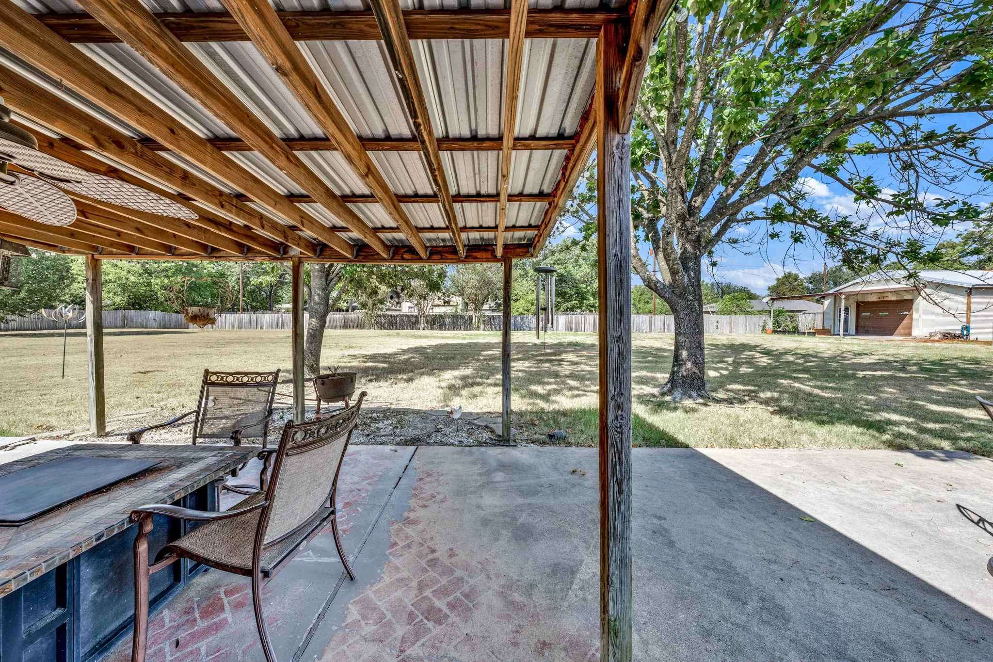 Covered patio with a wood-framed metal roof, concrete flooring, and an integrated brick accent