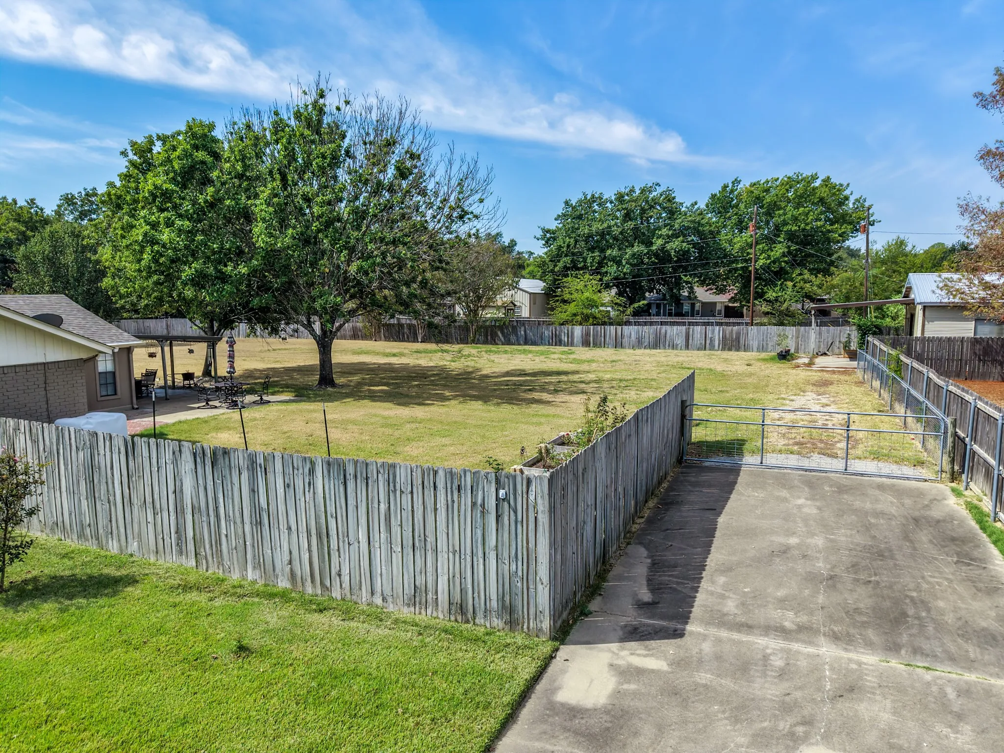 Expansive lot featuring mature trees, a wood privacy fence, and a concrete driveway