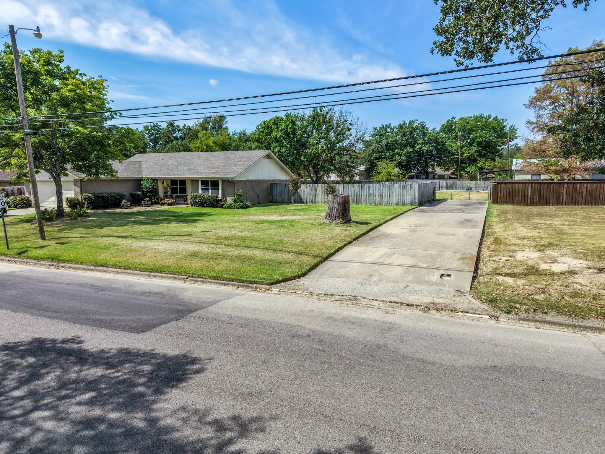 Exterior featuring a light brick facade, a concrete driveway, a wood fence, and a green lawn