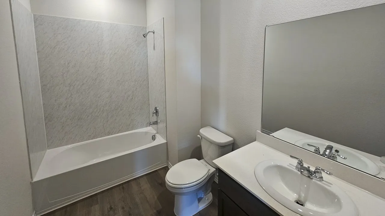 Full bathroom featuring a white porcelain tub with a patterned surround, a toilet, and a vanity with a white countertop and integrated sink