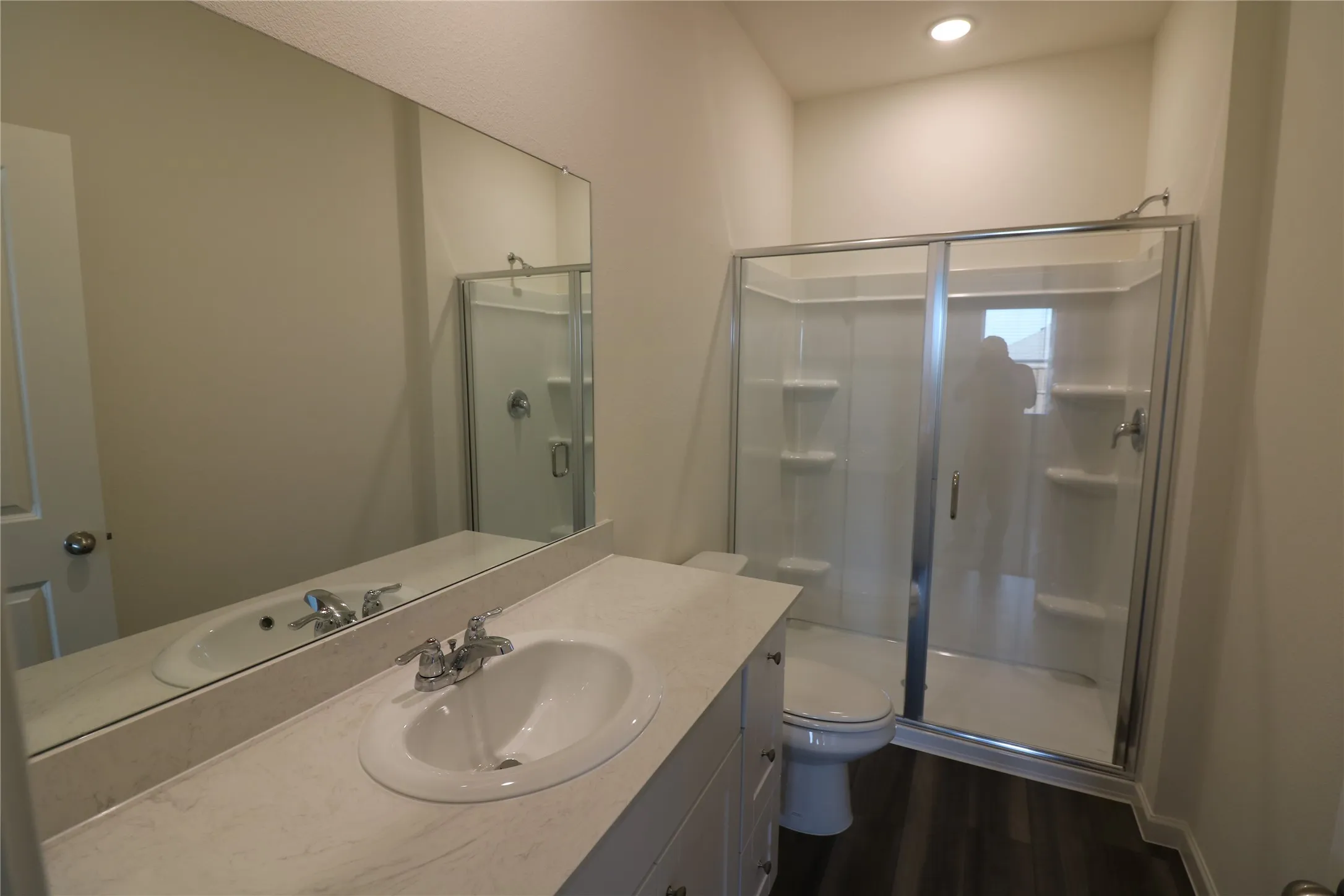 Vanity with integral sink, full-width mirror, enclosed shower with sliding glass door, and wood-finish flooring