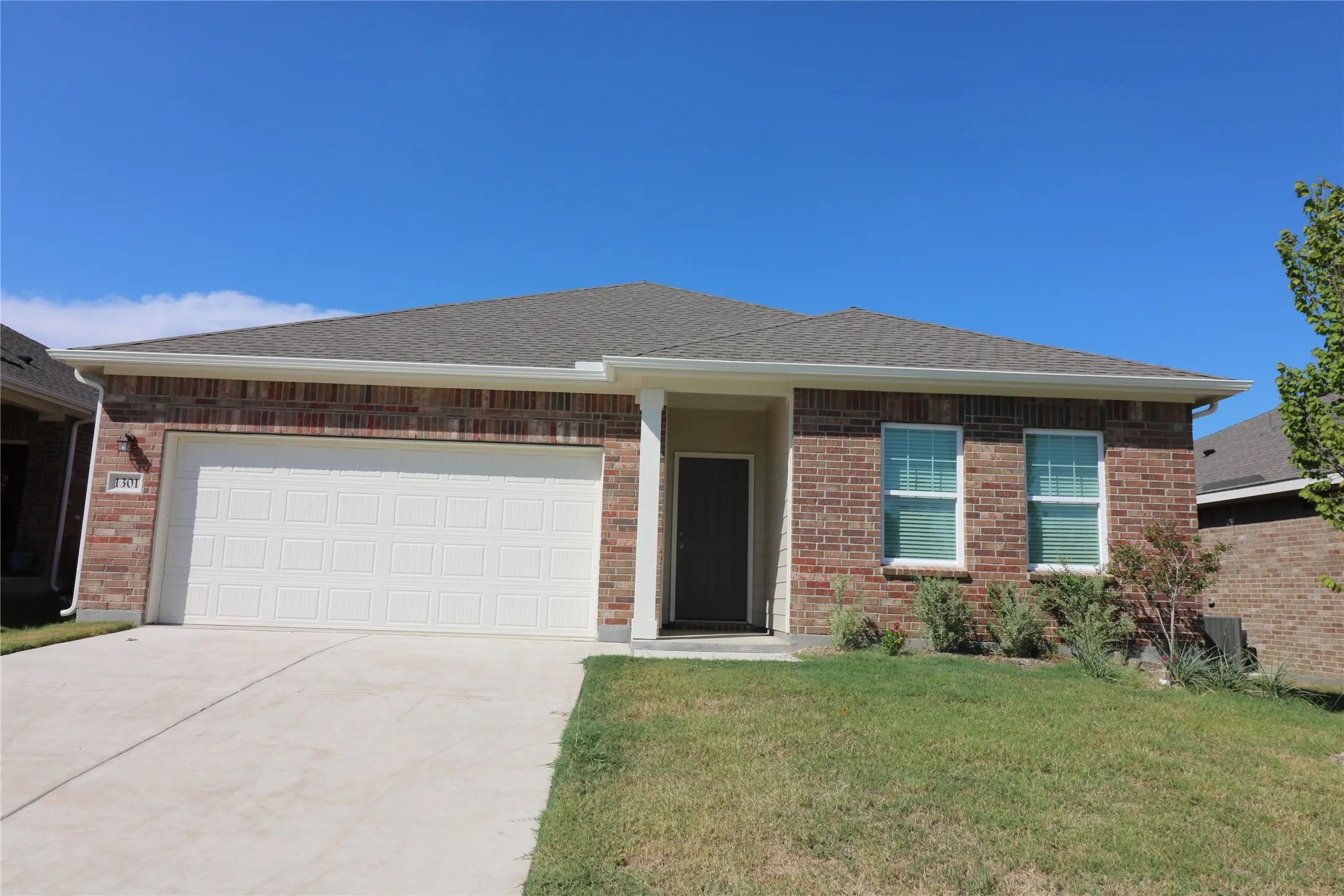 Brick exterior with an attached garage, concrete driveway, and a front entry door