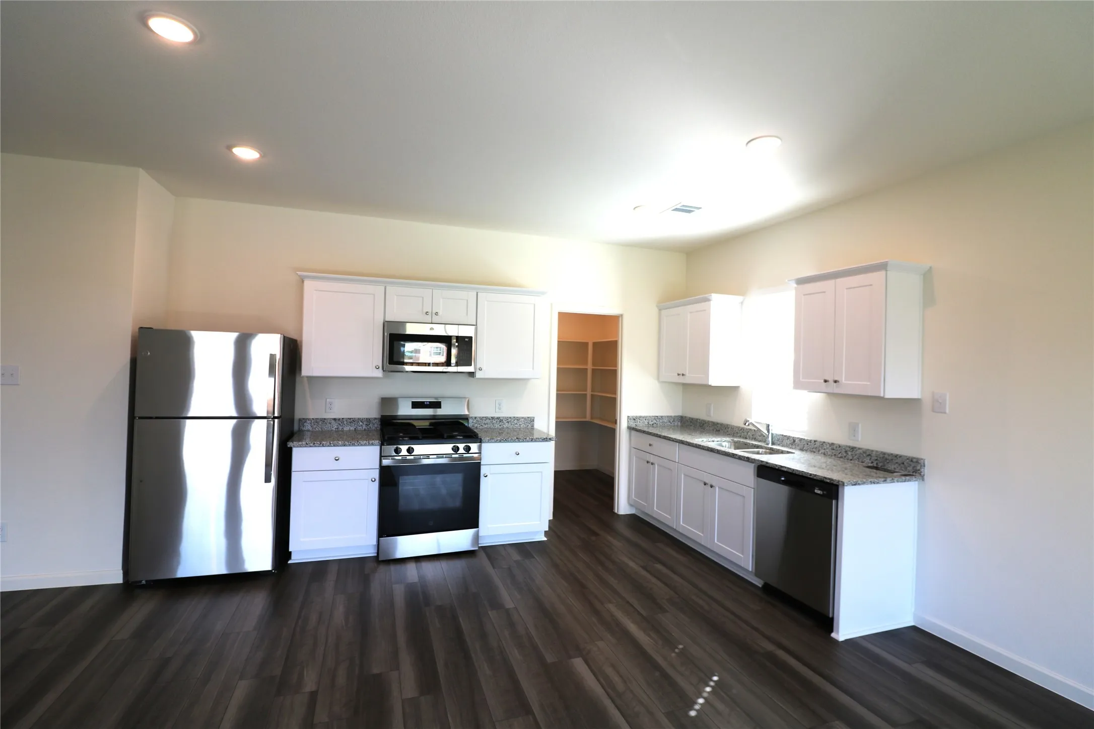 Kitchen featuring dark wood-finish flooring, white cabinetry, integrated stainless steel appliances, granite-style countertops, and recessed lighting