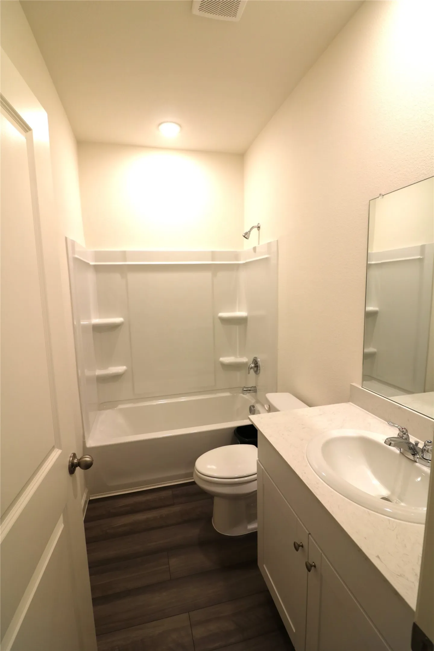 Bathroom featuring a white vanity with integrated sink, a white bathtub with shower, wood-finish flooring, and a flush-mount ceiling light