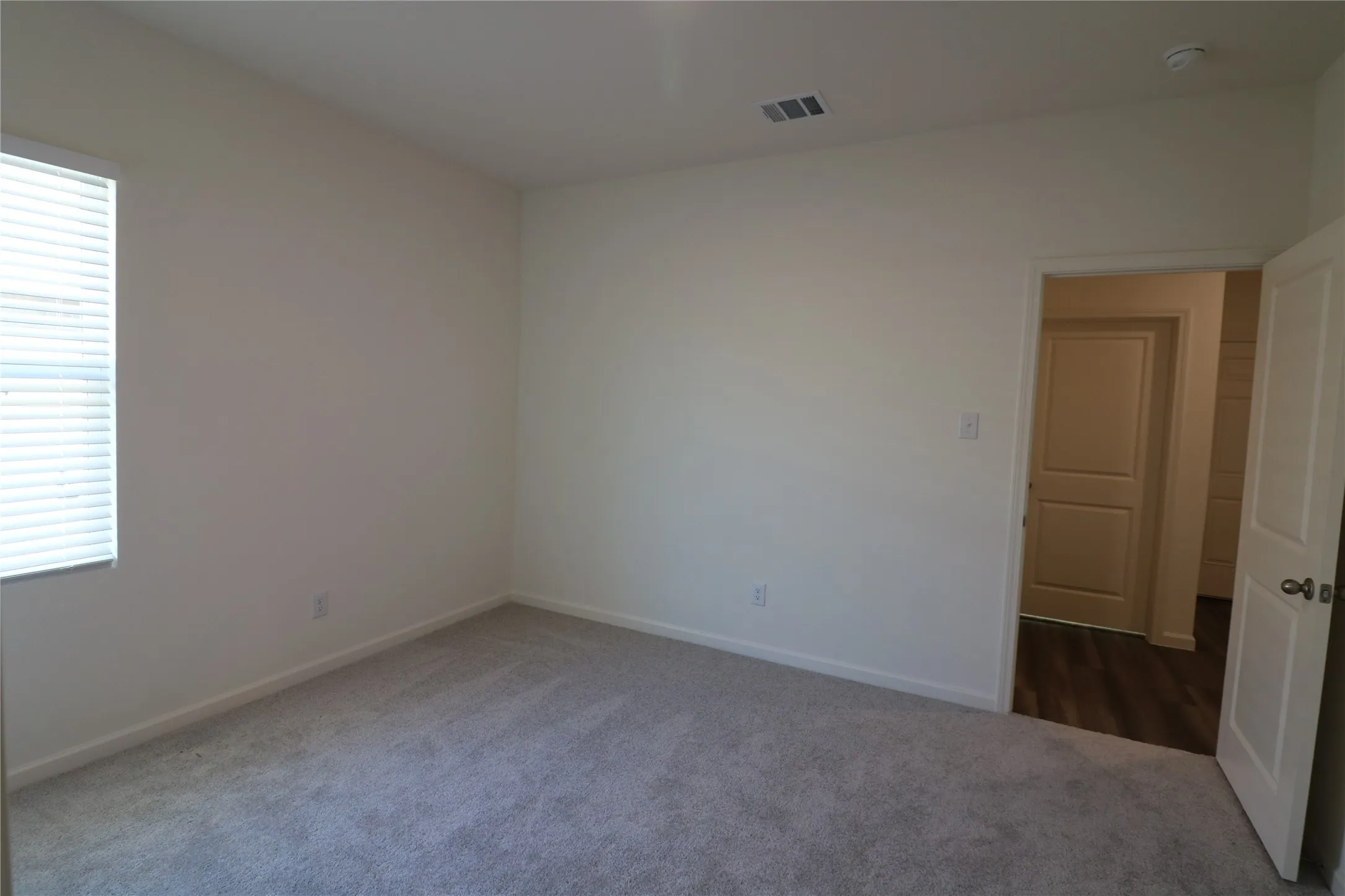 Carpeted flooring, neutral wall tones, window with blinds, white trim, and a paneled door with a brushed nickel knob