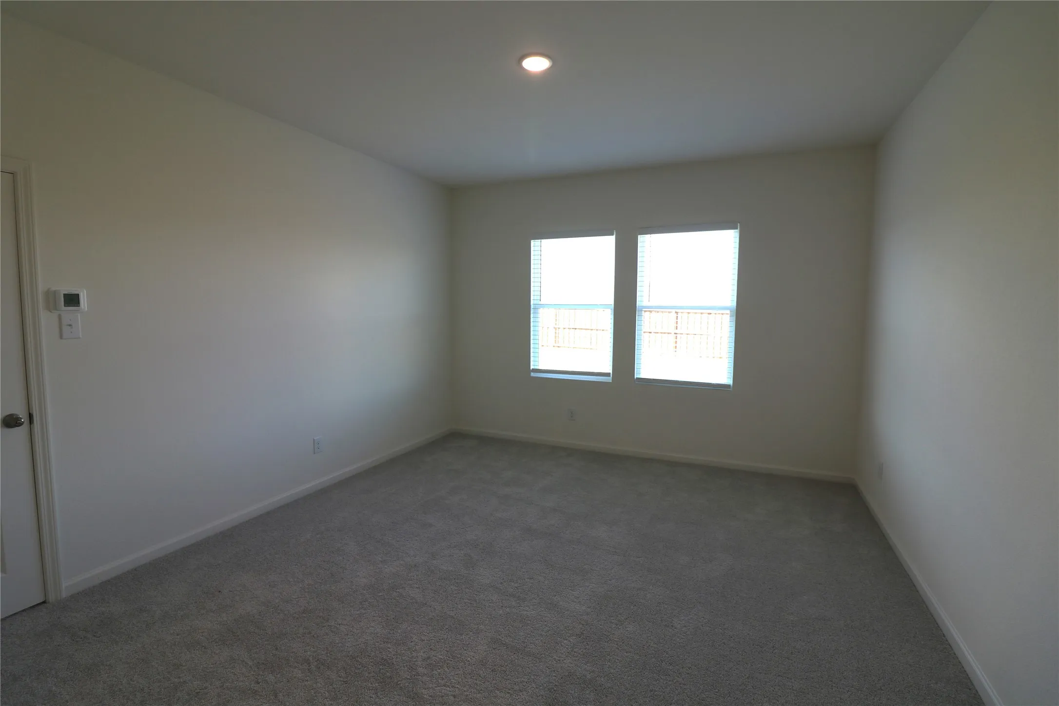 Neutral wall paint, recessed ceiling lighting, light gray carpeting, and two windows with blinds