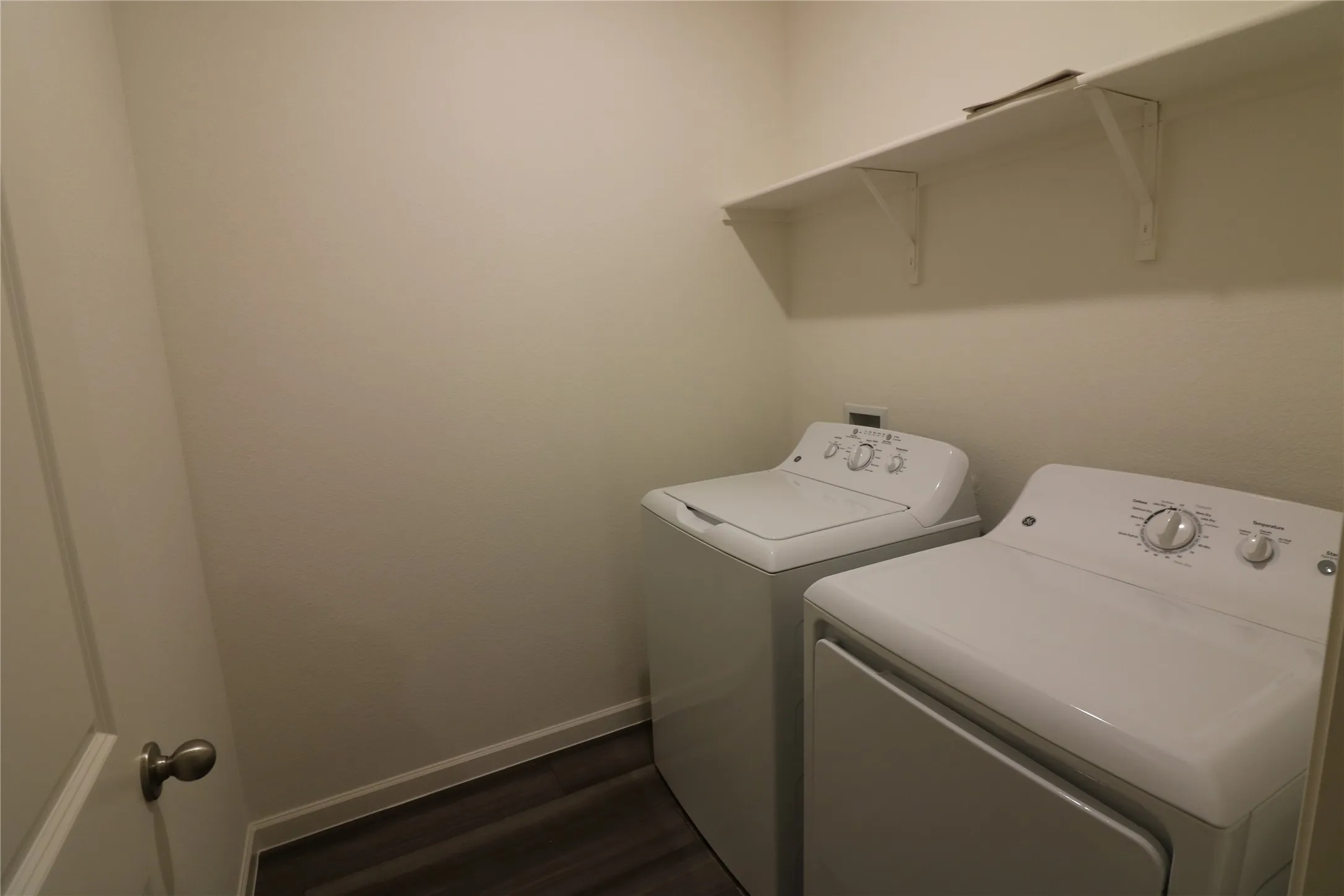 Dedicated laundry area with a white shelving unit, white walls, and wood-finish flooring