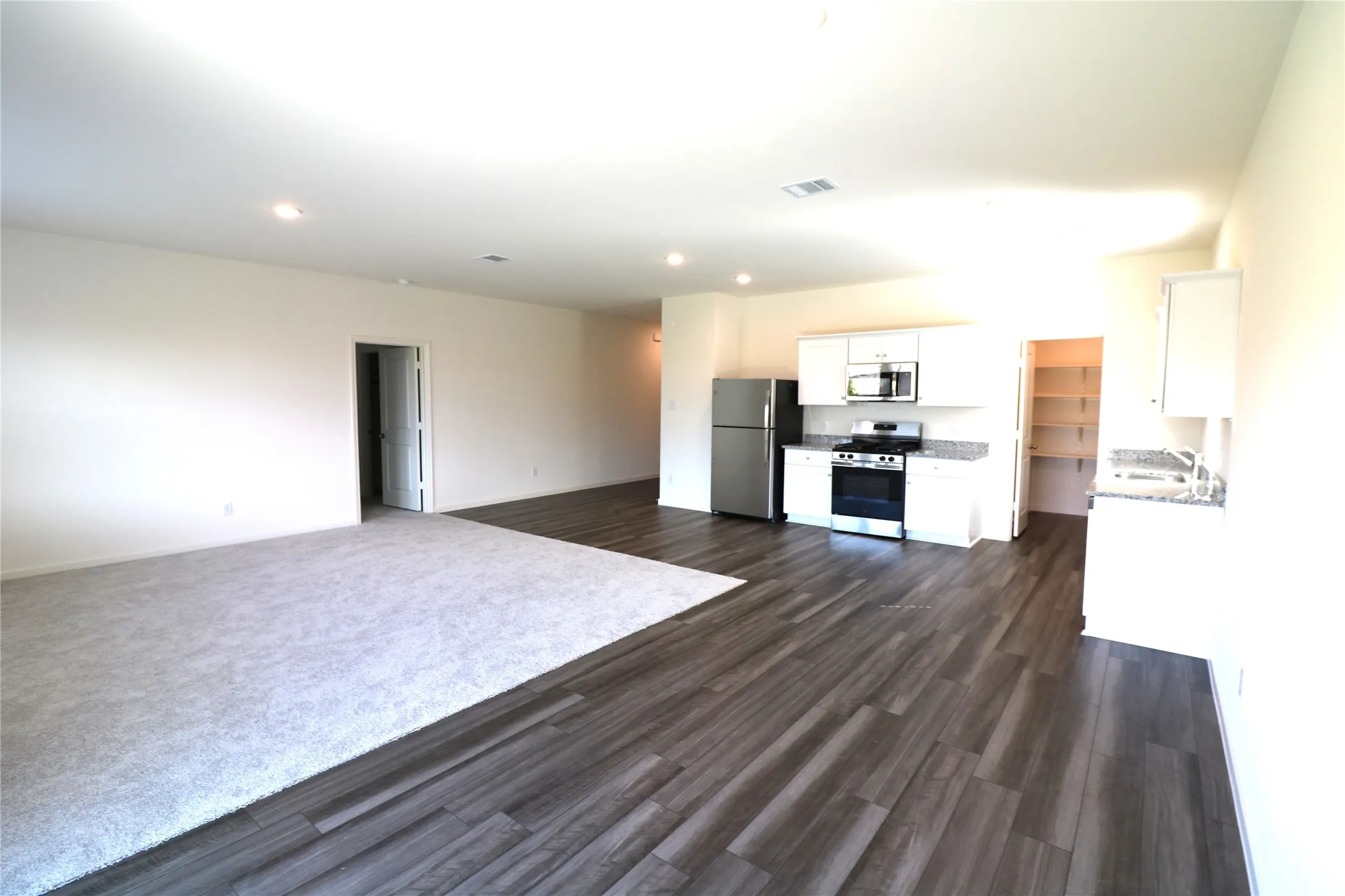 Open concept living area featuring wood-finish flooring, white cabinetry, and stainless steel appliances
