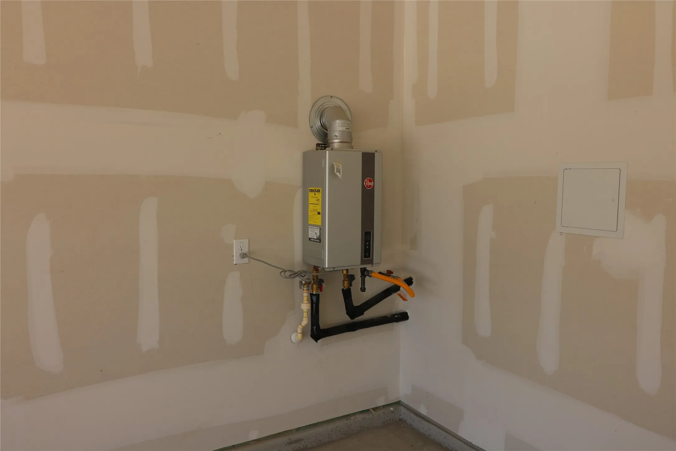 Wall-mounted tankless water heater with visible plumbing and an exhaust vent