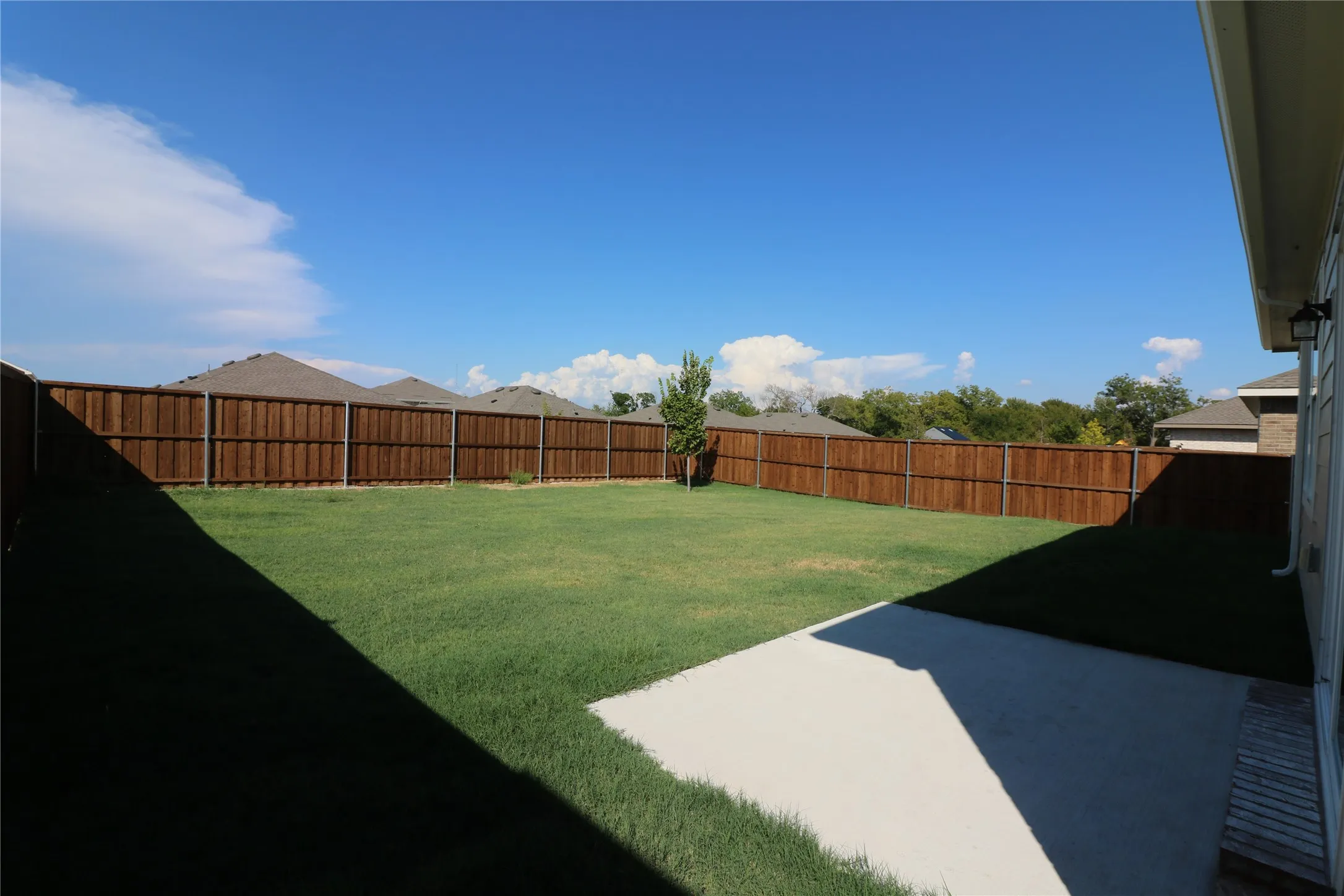 Expansive backyard featuring a manicured lawn, a full wood privacy fence, and a concrete patio