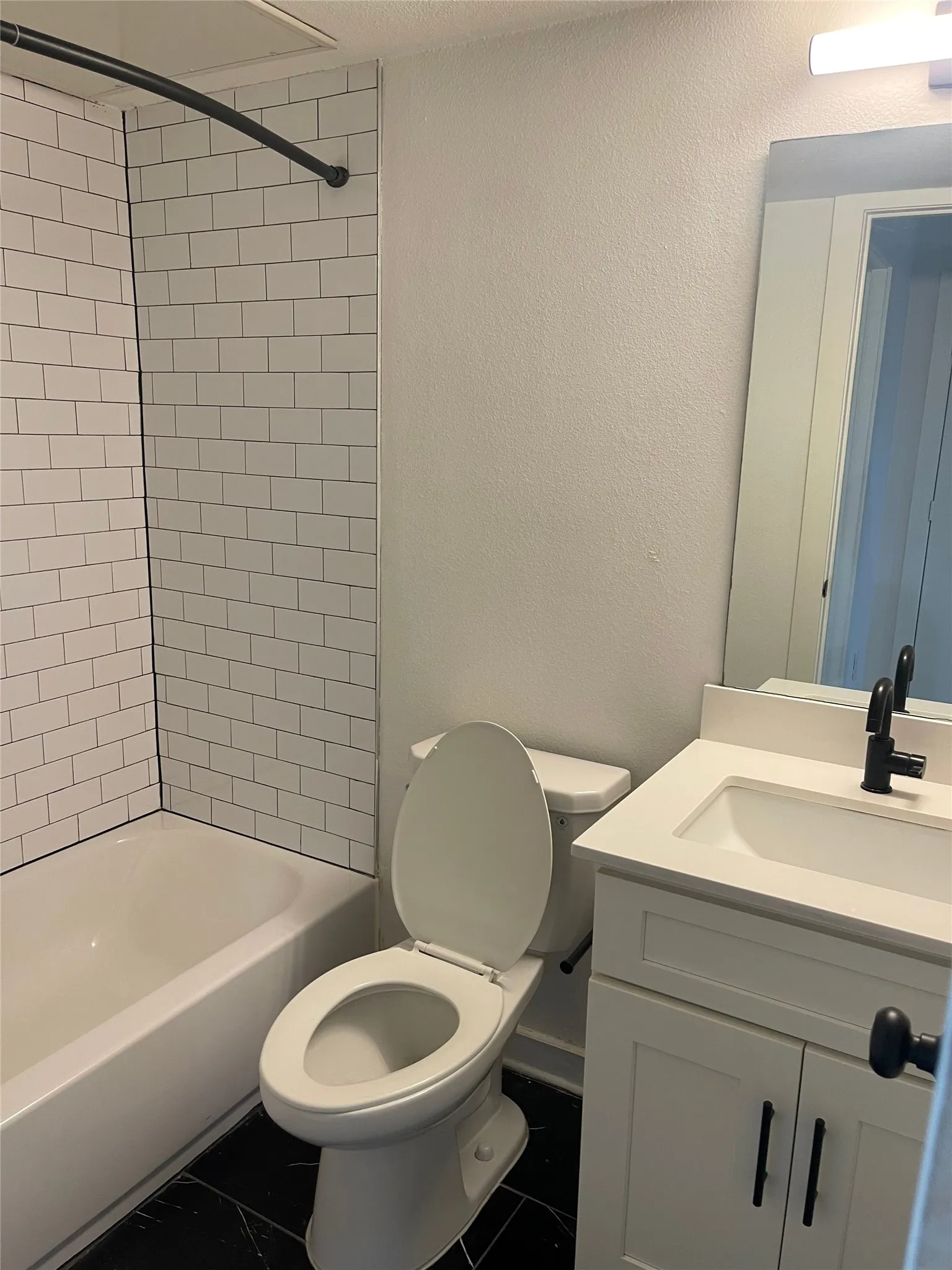White subway tile shower surround, black-finish fixtures, white vanity cabinet, white countertop, and dark floor tiling