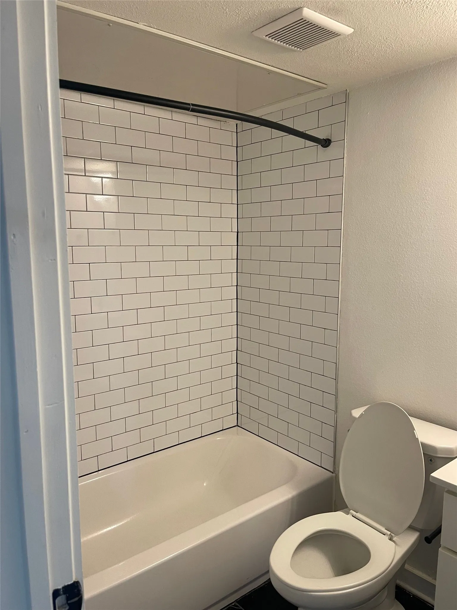 Tub/shower combination featuring white subway tile surround and a curved shower rod