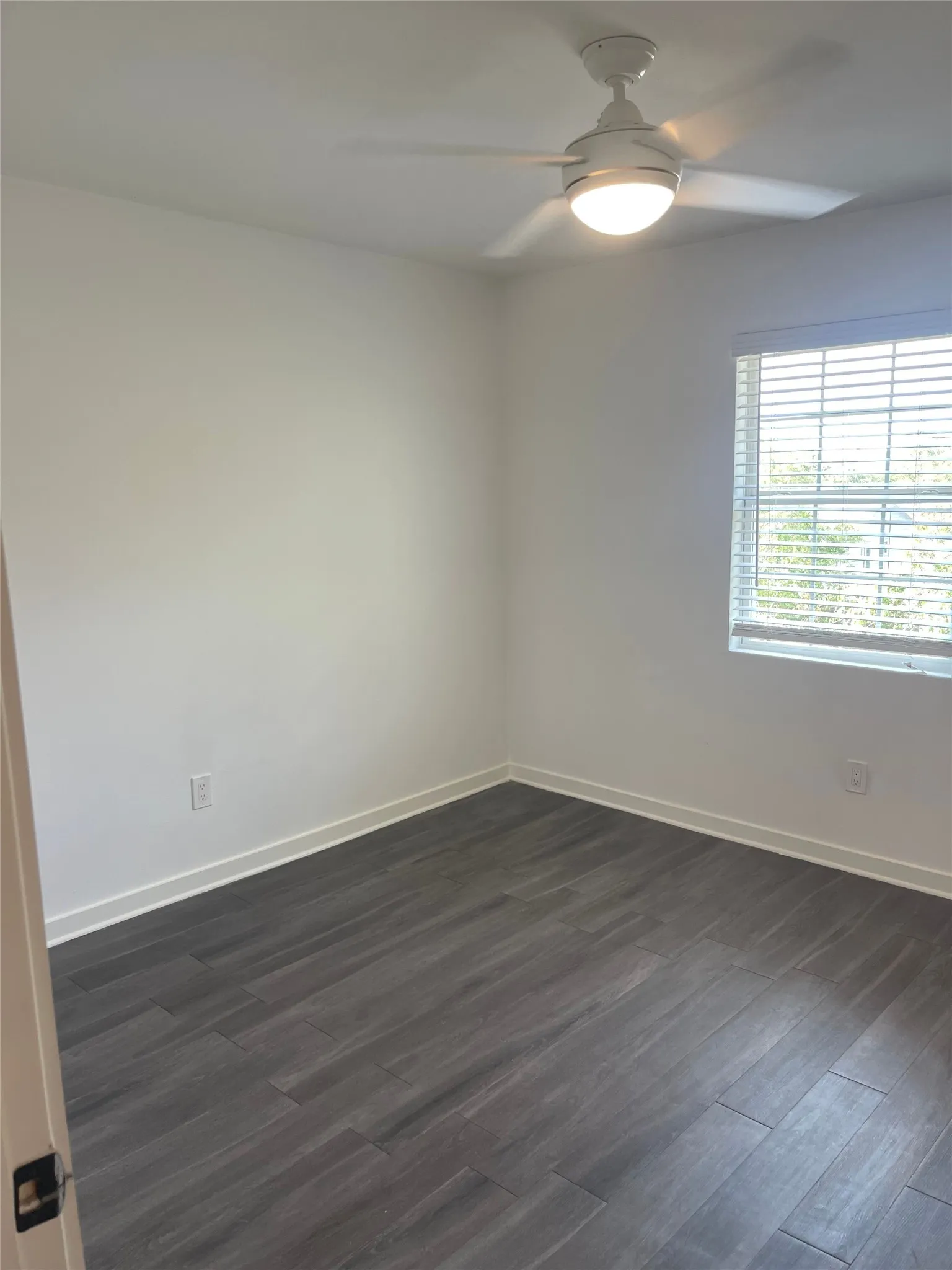 Wood-finish flooring, white walls, window with blinds, and ceiling fan with integrated lighting
