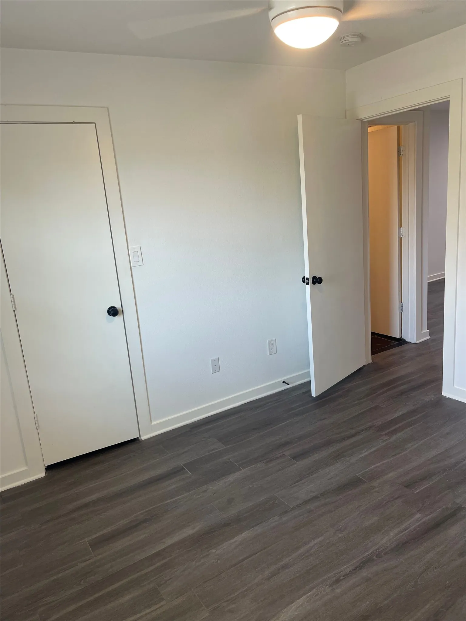 Wood-finish flooring with white walls and trim, featuring a ceiling fan with integrated lighting