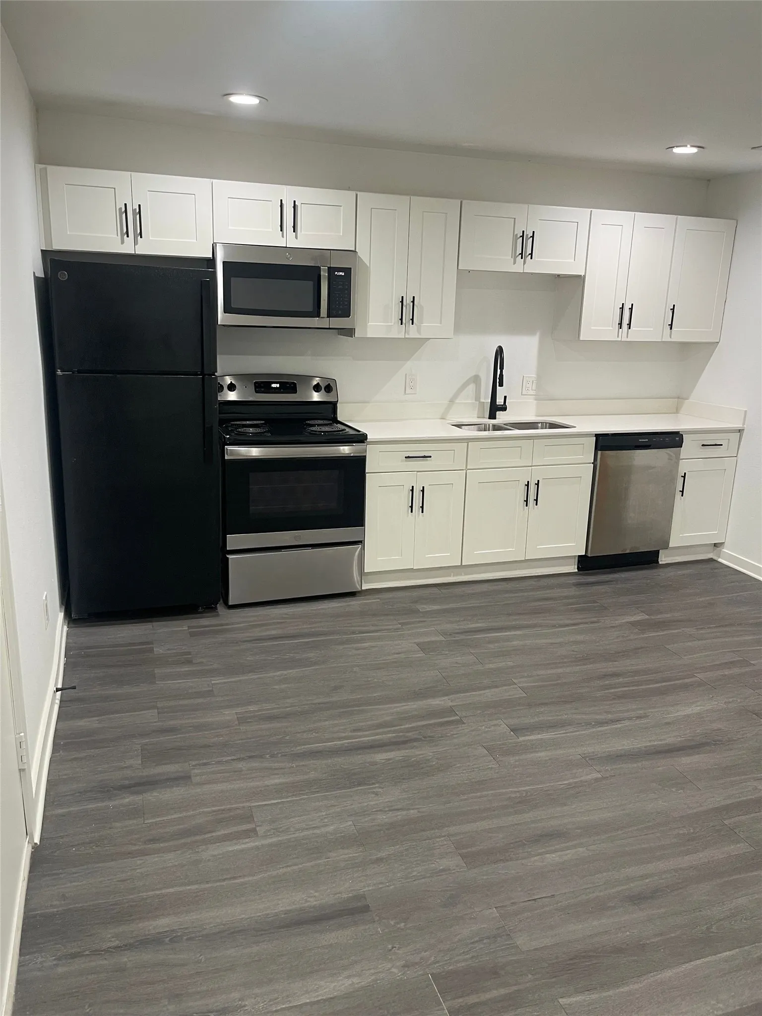 Kitchen featuring white shaker cabinetry, stainless steel appliances, a black refrigerator, light-toned countertops, and wood-finish flooring