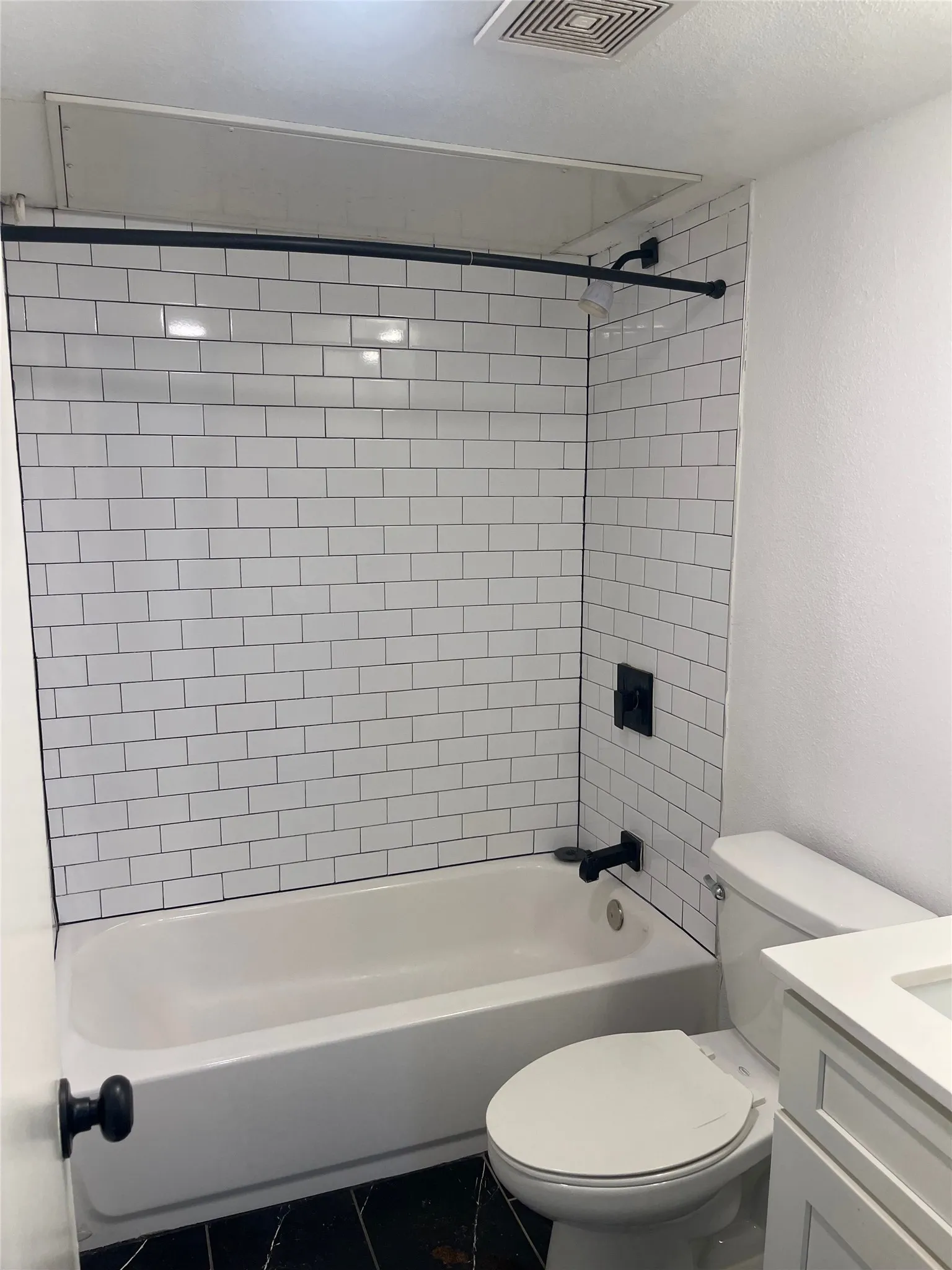 Bathtub with subway tile surround, black matte fixtures, and black tile flooring