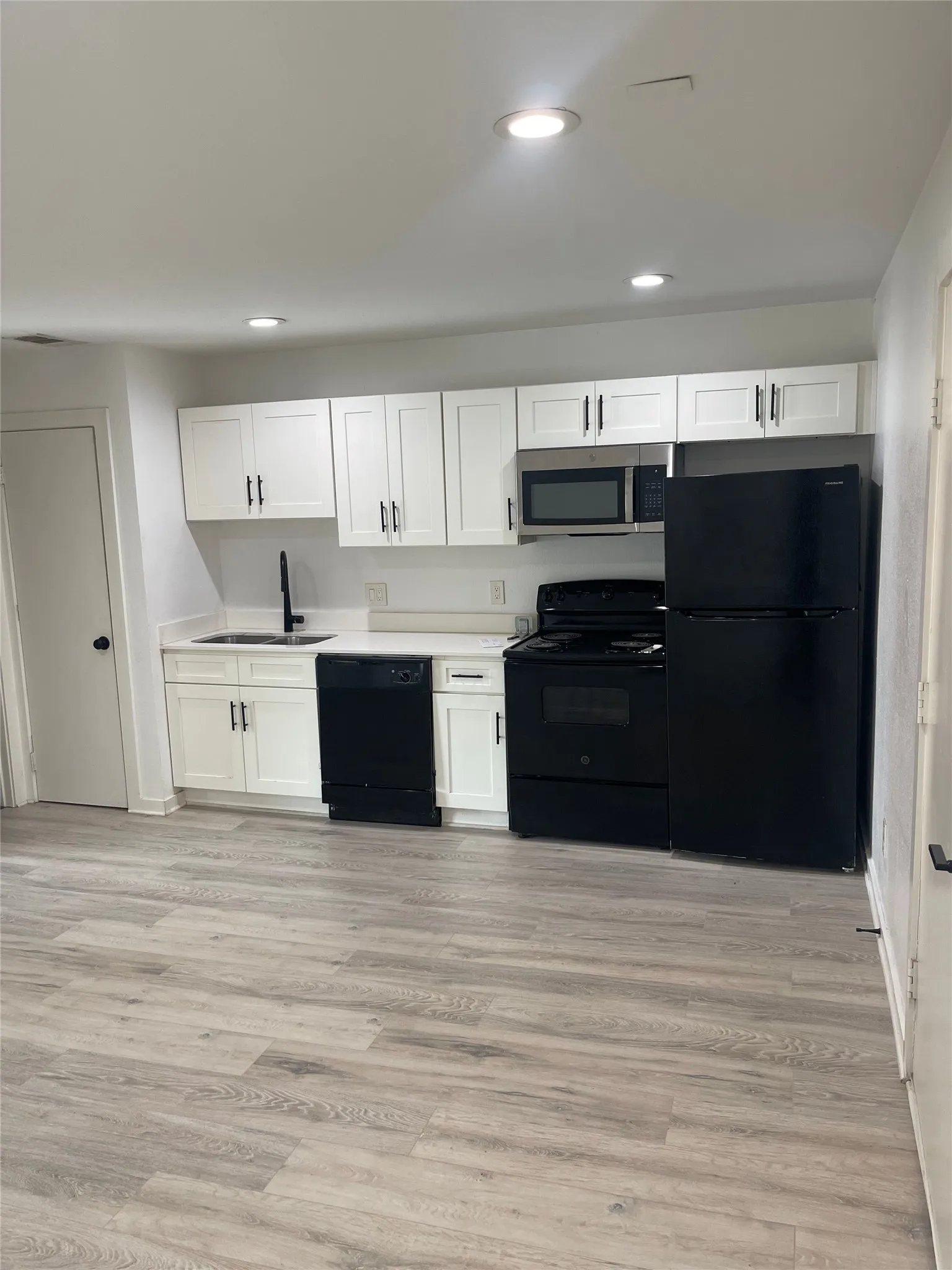 Kitchen featuring white shaker cabinetry, white countertops, stainless steel sink with matte black faucet, and a suite of black appliances including a refrigerator, dishwasher, and range