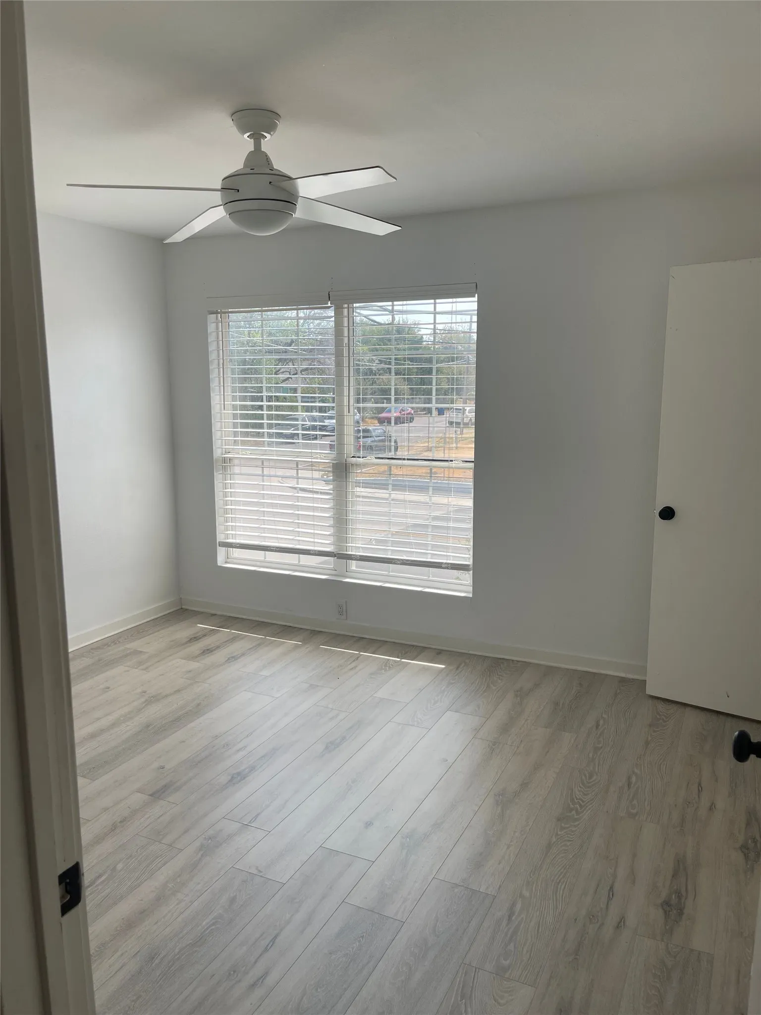 White ceiling fan, window with blinds, wood-finish flooring, and white interior walls