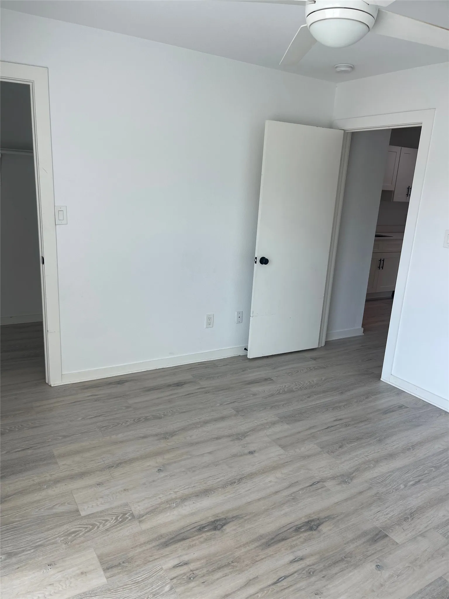 Wood-finish flooring, white walls, white ceiling fan, and white doors