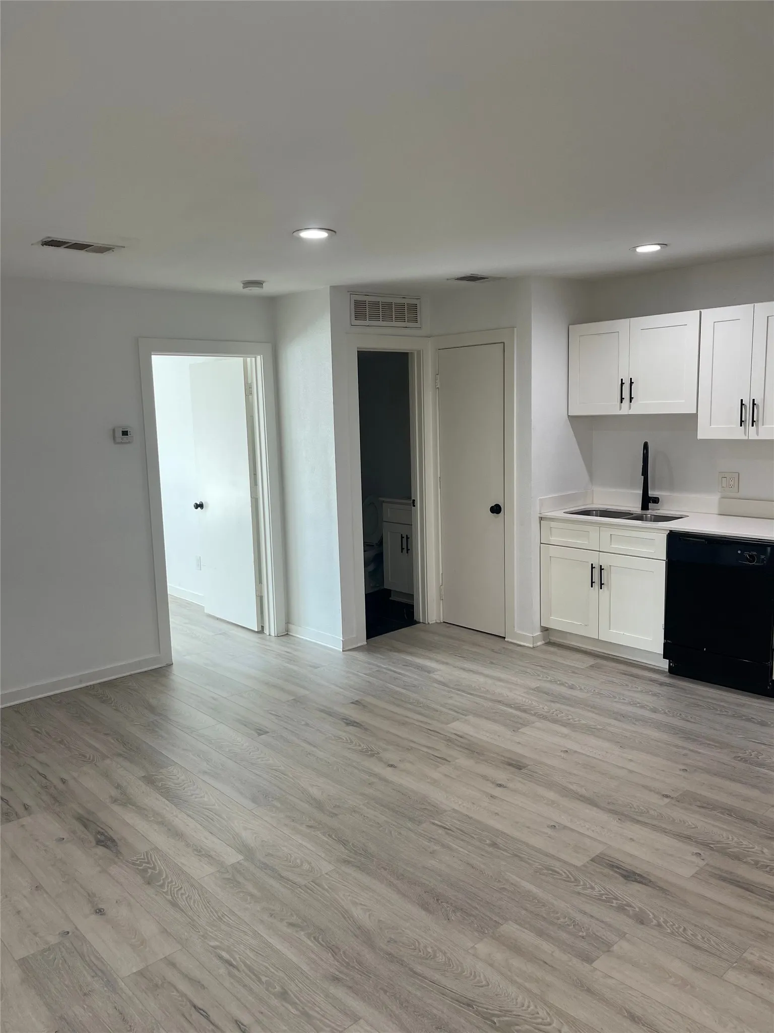 Recessed ceiling lighting, wood-finish flooring, white cabinetry with black hardware, black dishwasher, and a black faucet