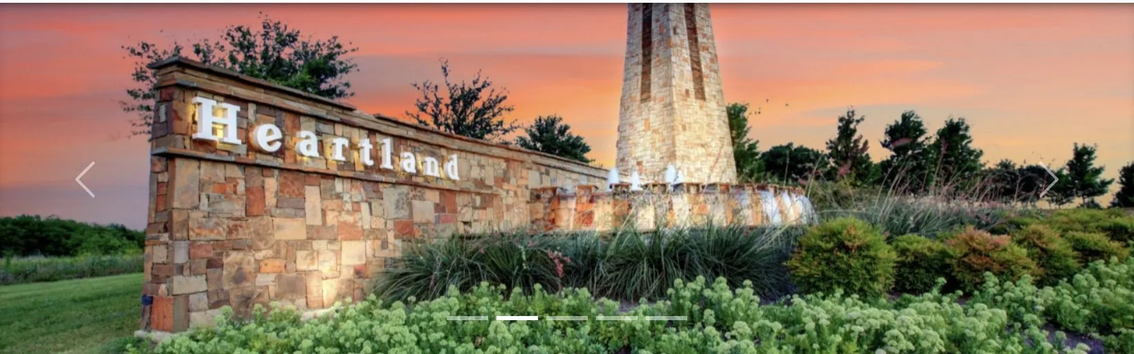 Stone veneer entryway monument with illuminated lettering, featuring a stone tower and landscaped greenery