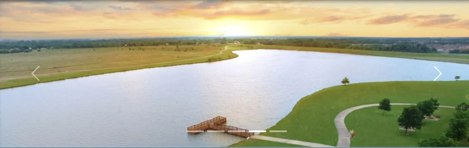 Expansive lake with a dock, surrounded by lush green lawns and a paved walking path