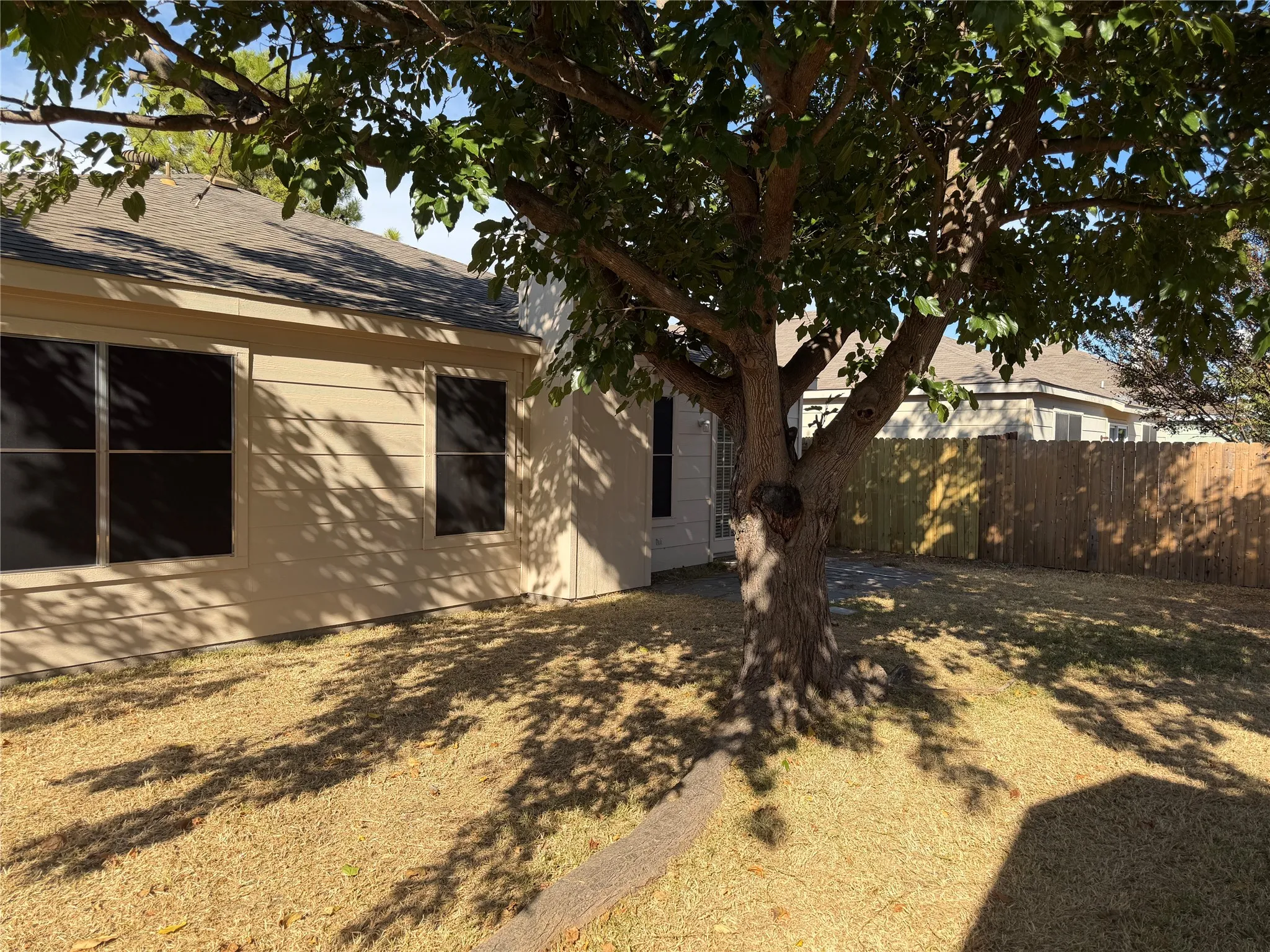Expansive backyard with a large mature tree, wood fencing, and a neutral-toned exterior