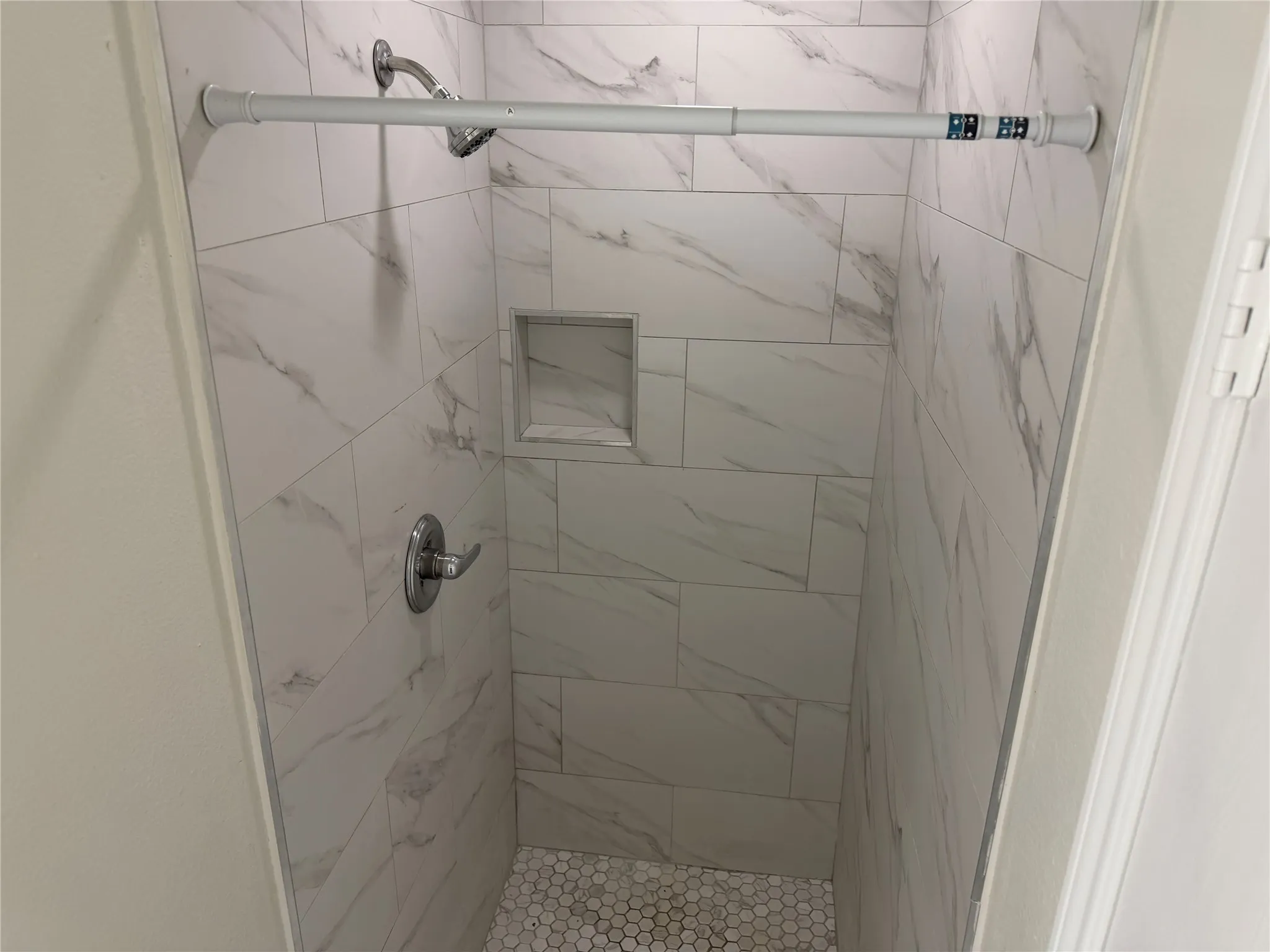 Tile shower featuring a recessed niche, chrome fixtures, and a white penny tile floor
