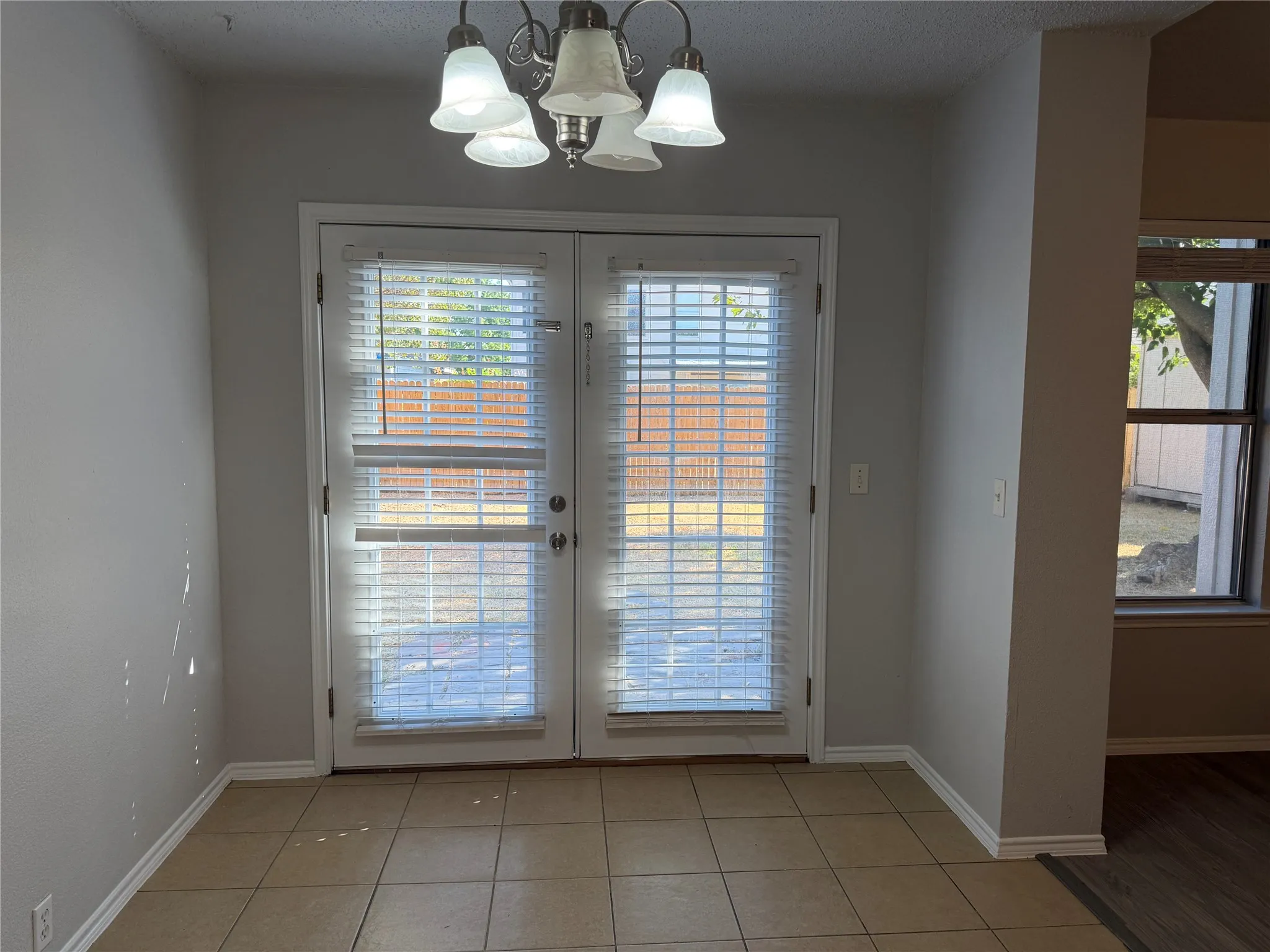 Double French doors with integrated blinds, ceramic tile flooring, and a multi-light chandelier