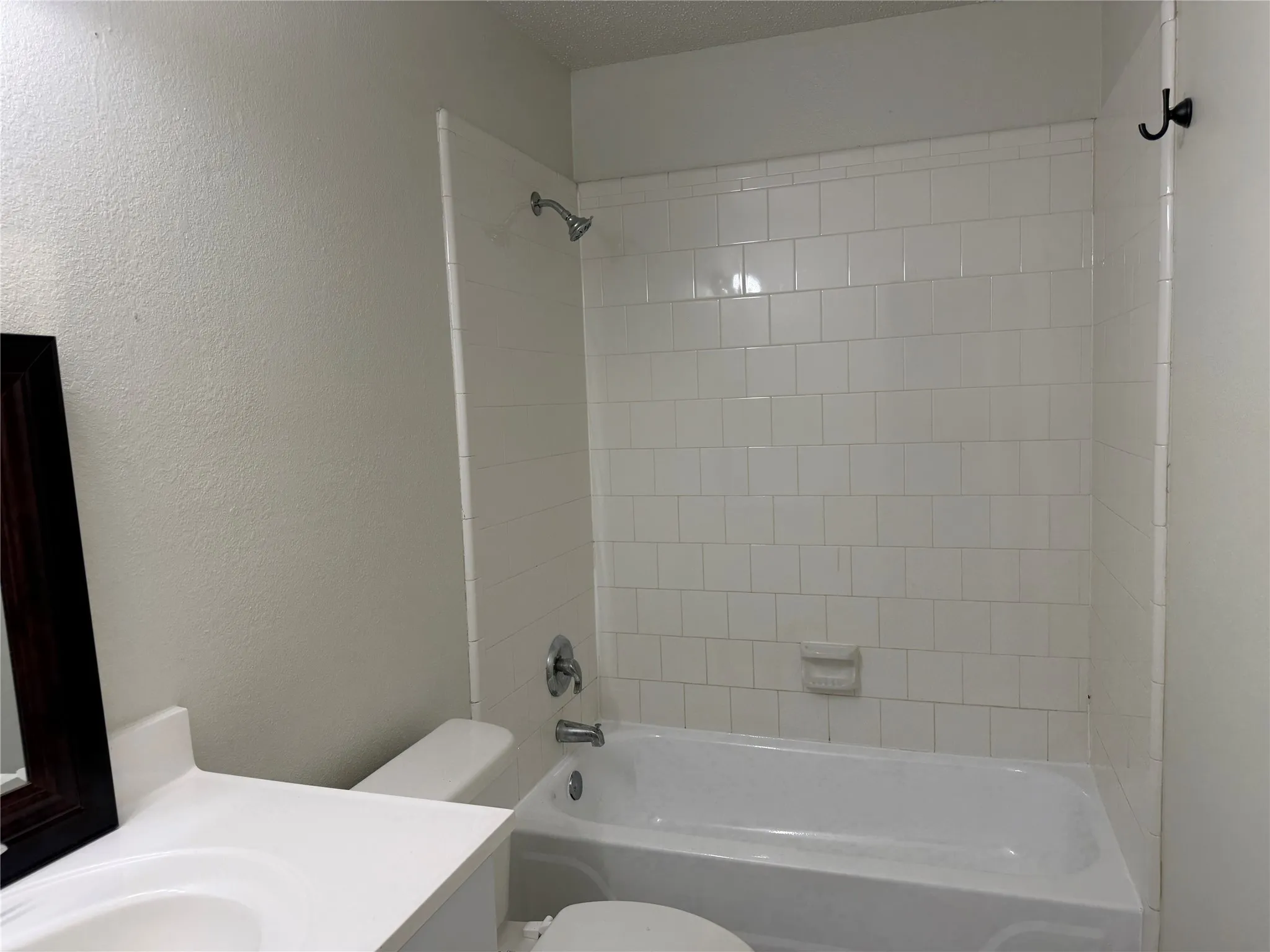 White tile shower surround with chrome fixtures, integrated bathtub, and a white vanity with an undermount sink