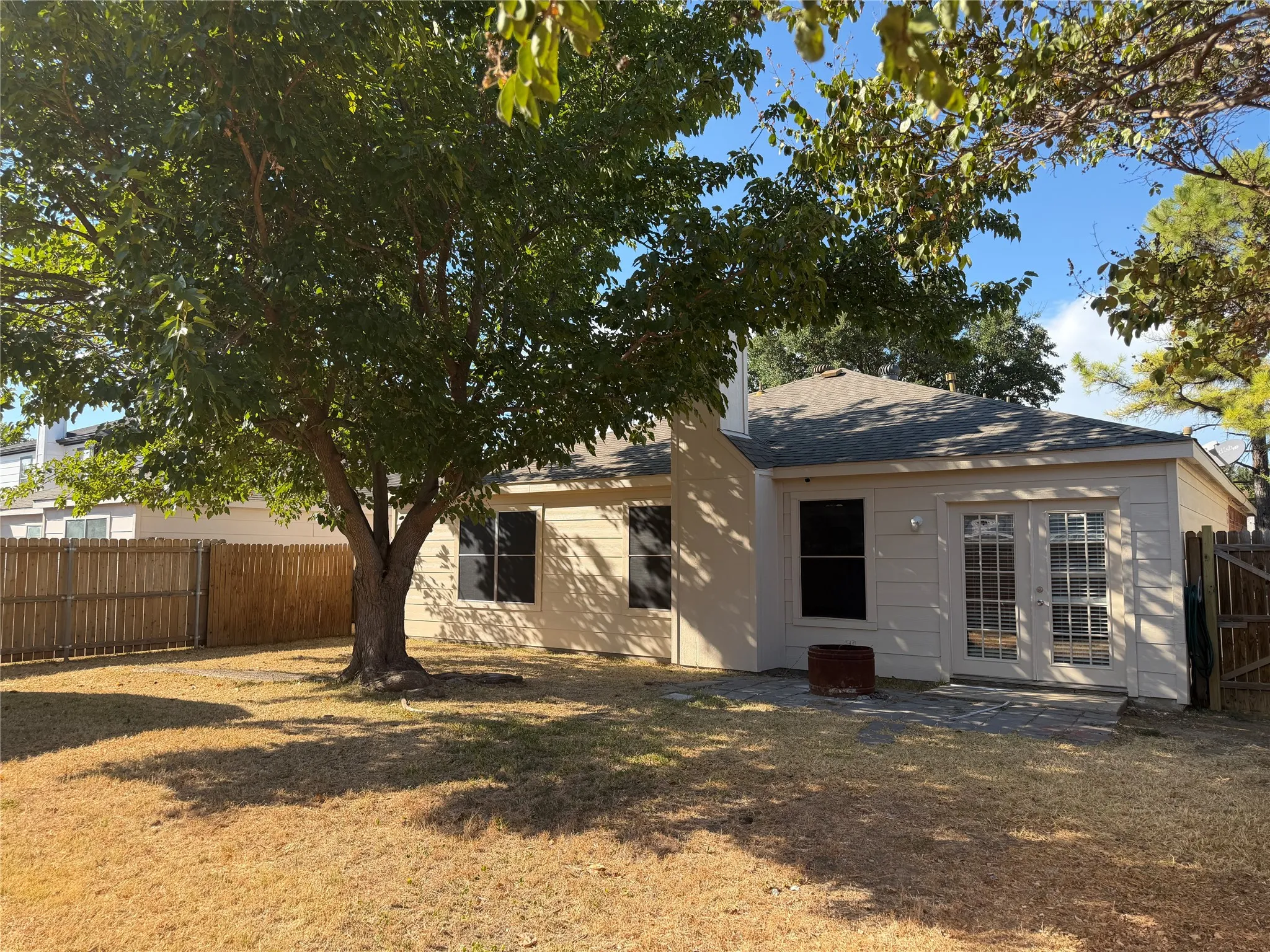 Expansive backyard featuring a mature tree, privacy fencing, and a paver patio with double French doors