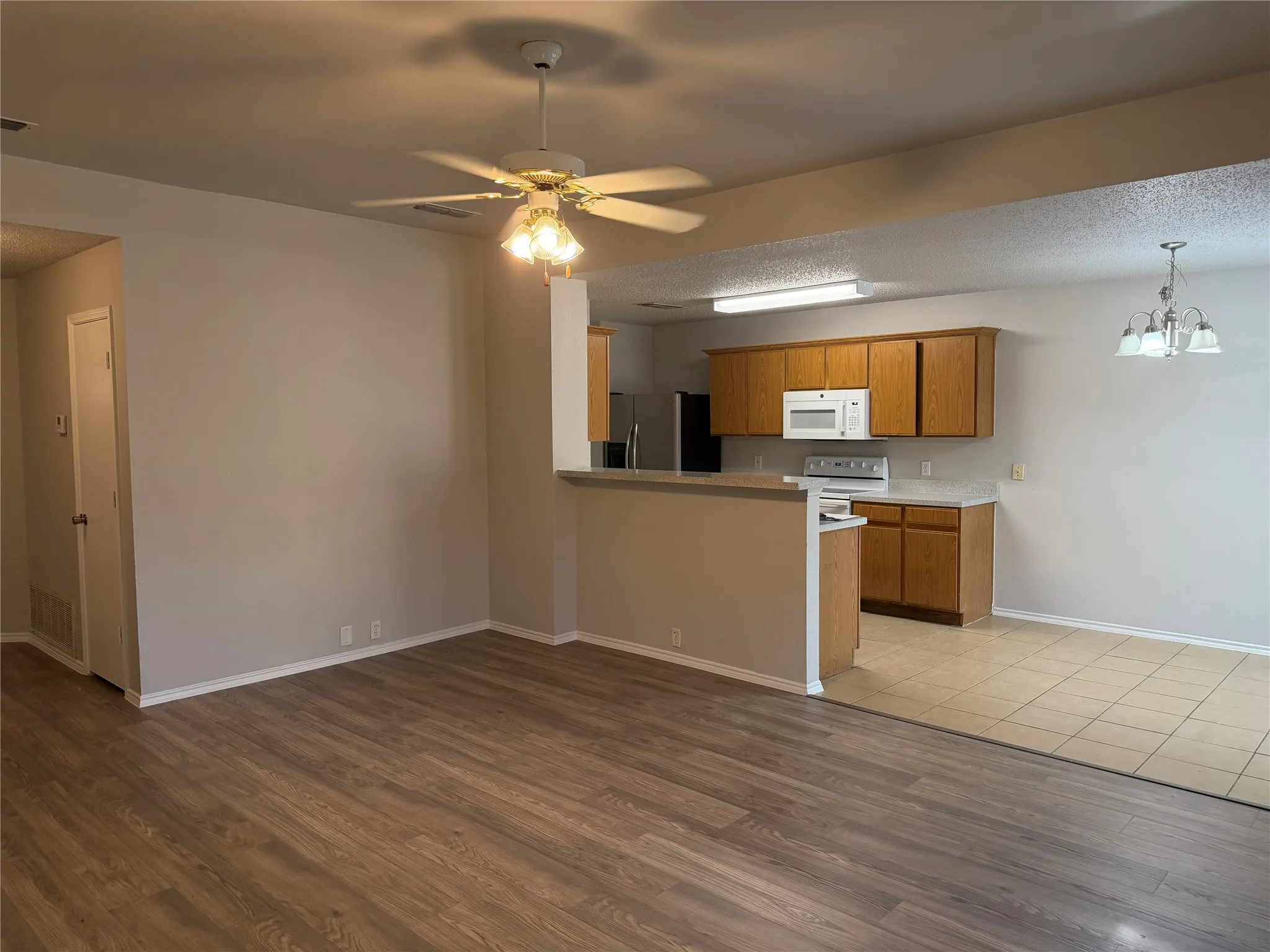 Wood-finish flooring, ceiling fan with integrated lighting, kitchen featuring wood cabinetry, white countertops, and white appliances, and a tiled dining area