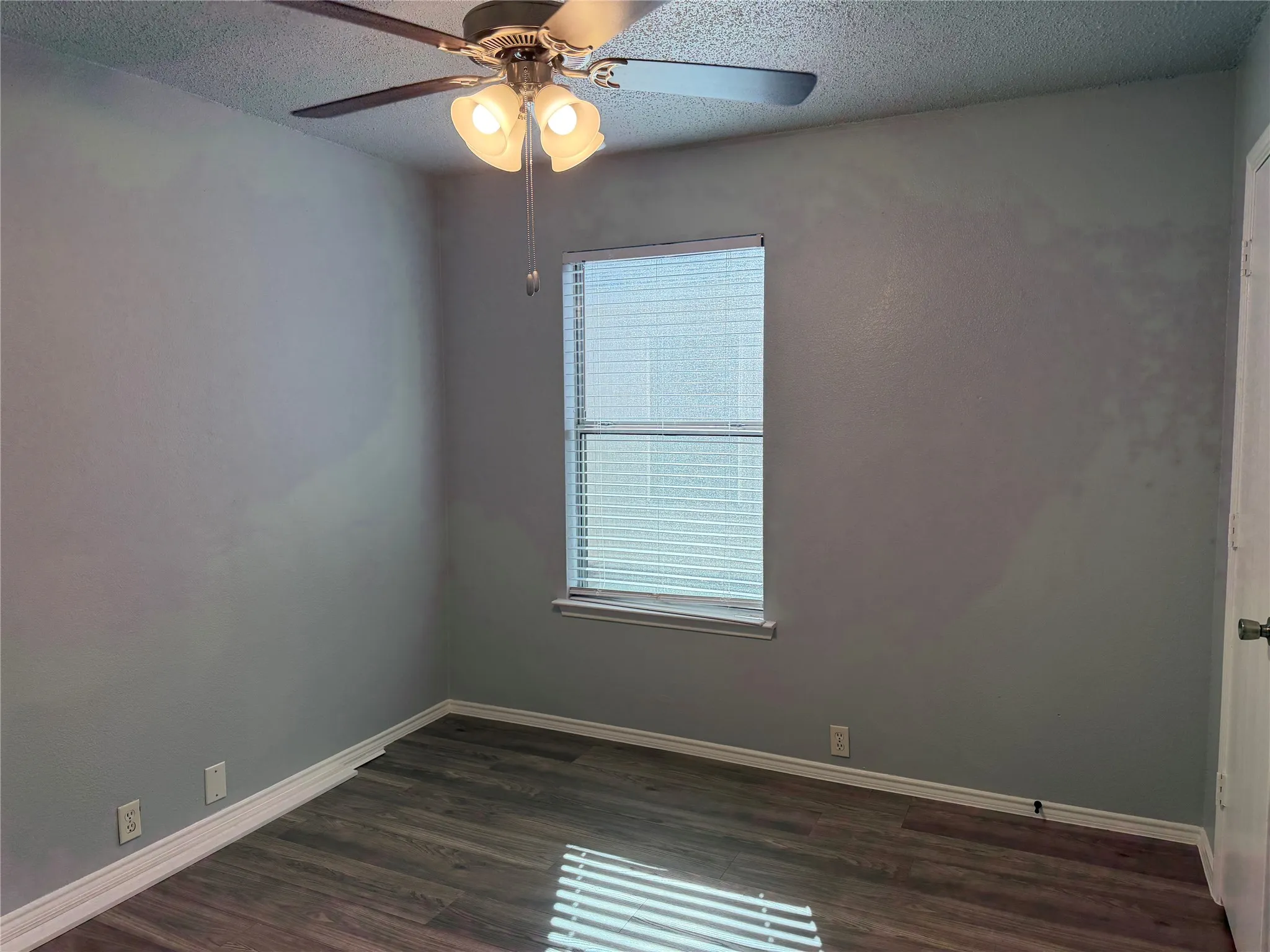Wood-finish flooring with white trim and a window with blinds