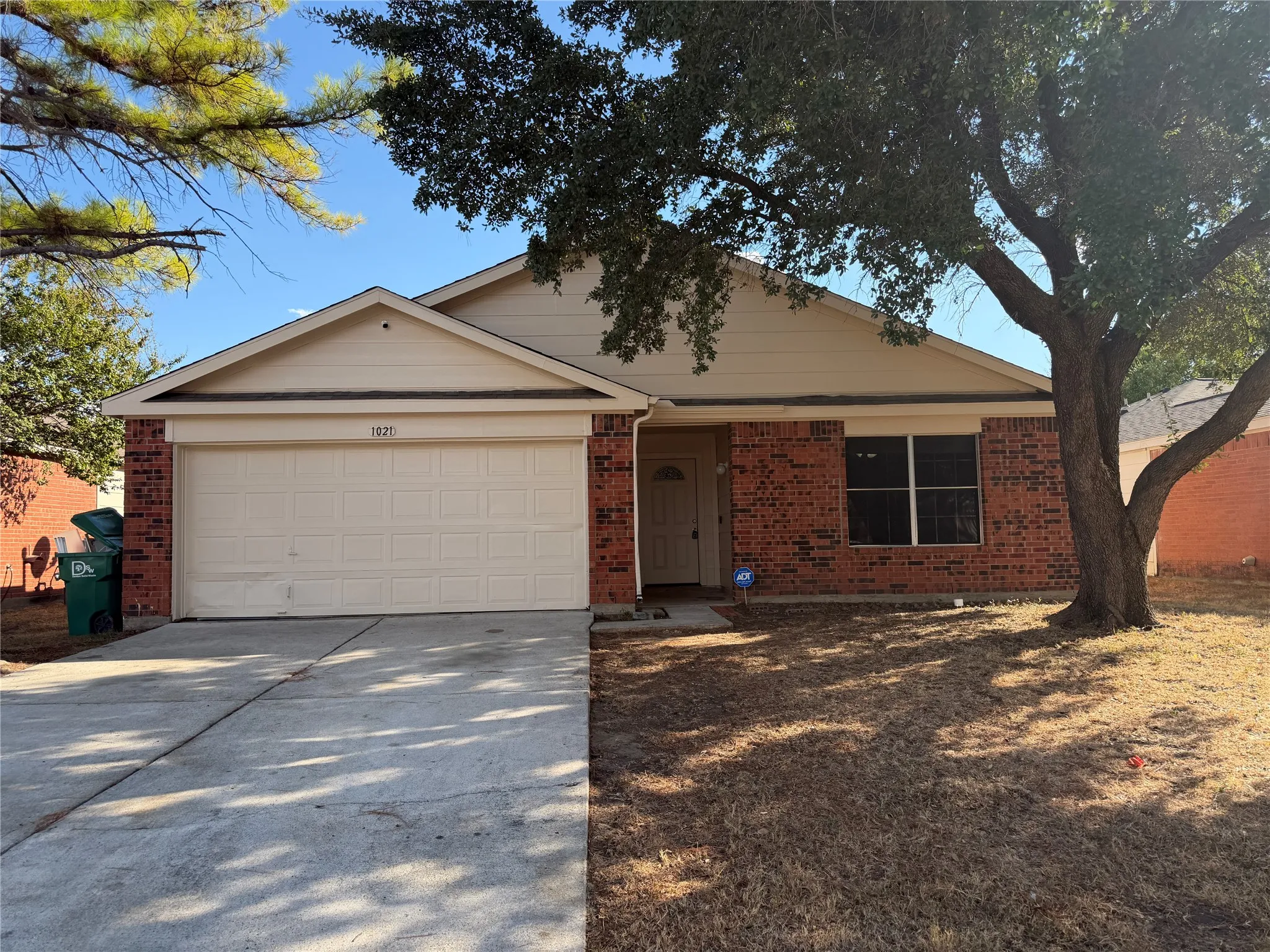 Brick facade with siding accents, attached garage, concrete driveway, and mature tree