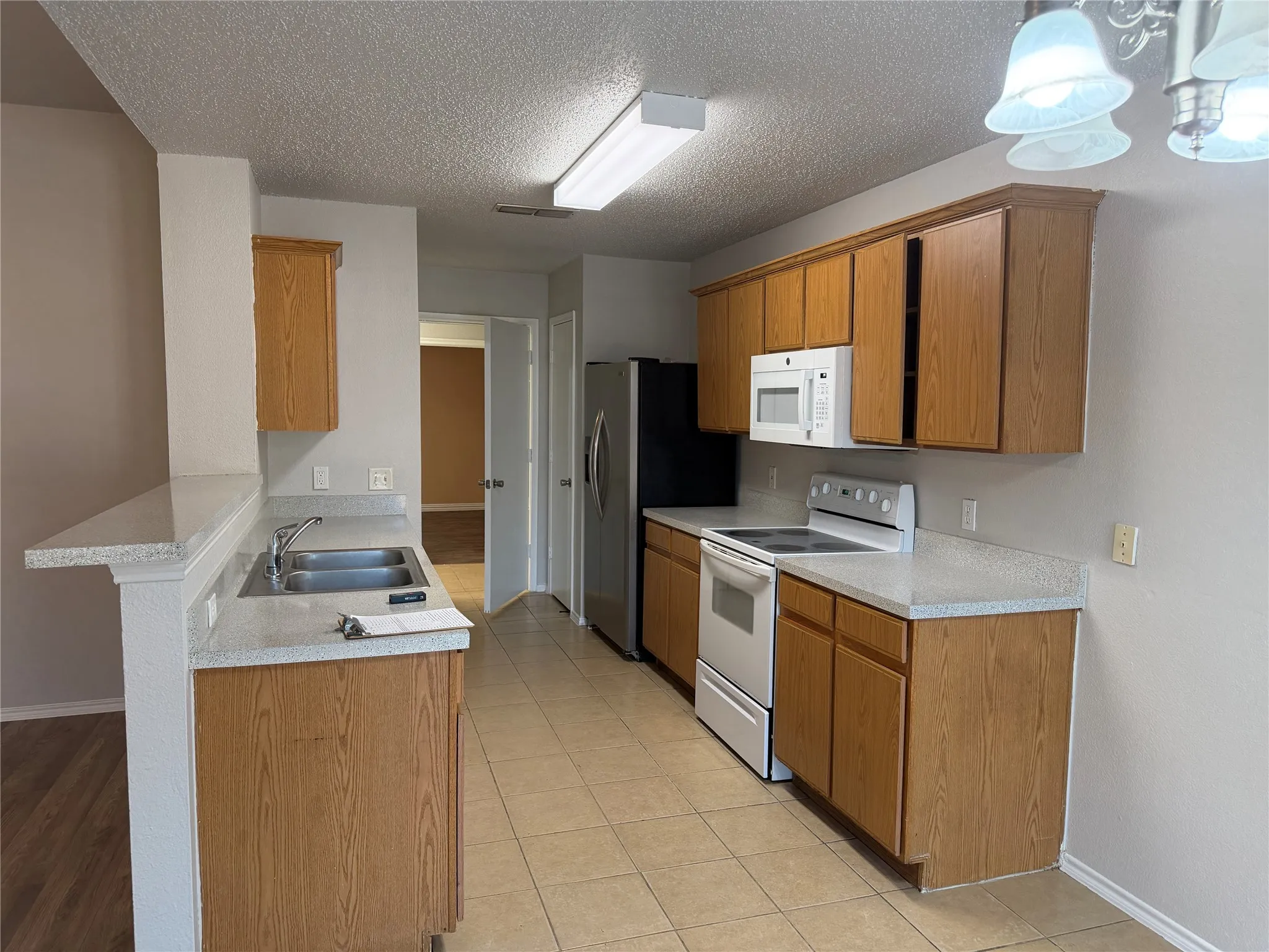 Kitchen featuring wood cabinetry, white countertops, tile flooring, and a double basin stainless steel sink