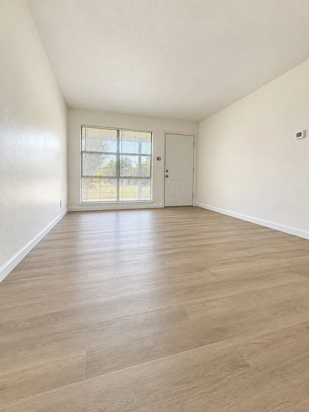 Light-toned wood-finish flooring, white walls, and a large multi-pane window