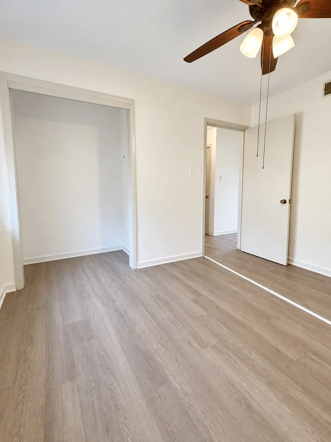Wood-finish flooring, white painted walls, and a ceiling fan with integrated lighting