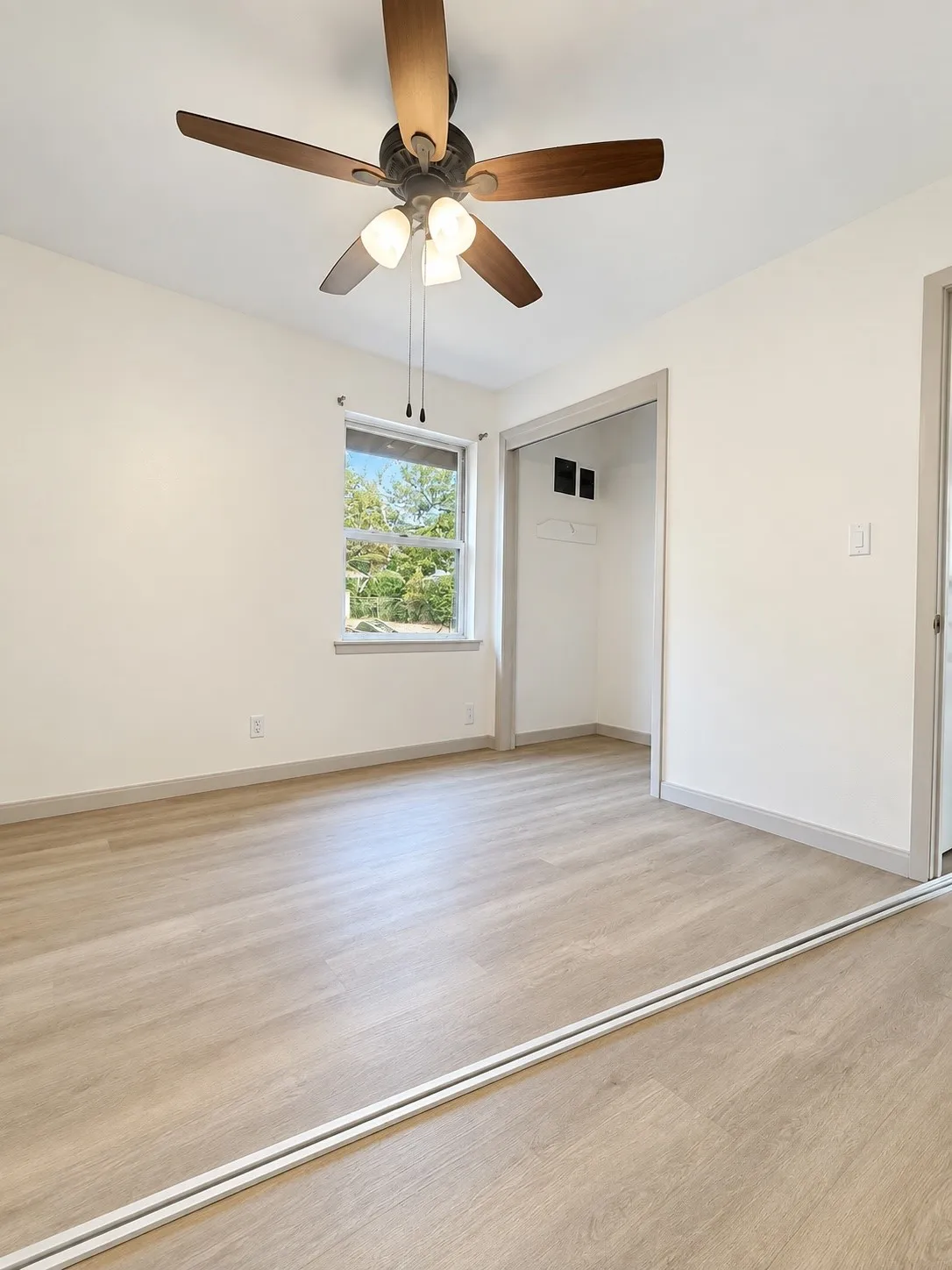 Wood-finish flooring with a ceiling fan light fixture, bright window, and an open closet space